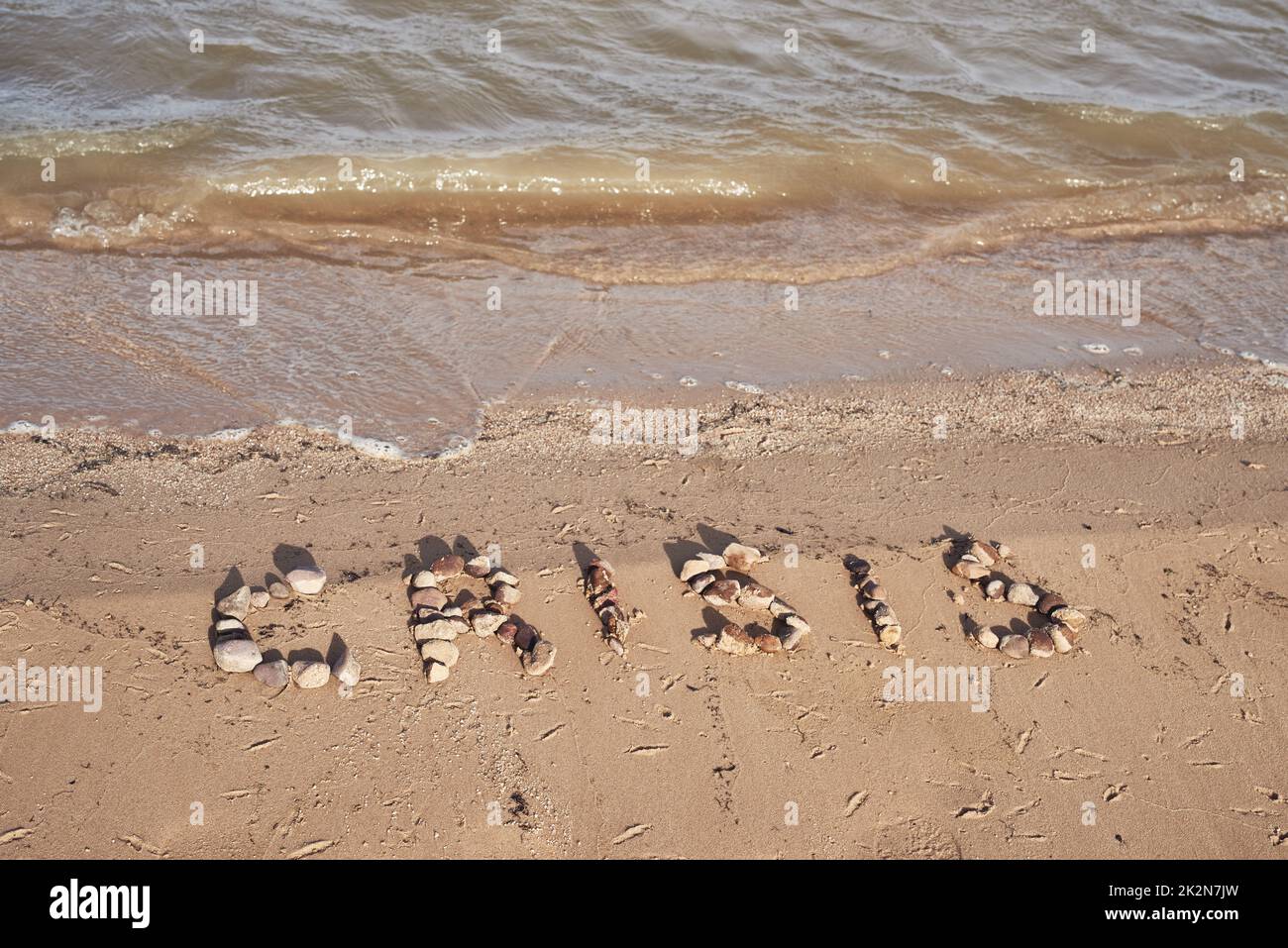 Nessun'altra parola per descrivere la situazione. Colpo della crisi parola scritto sul terreno con piccole pietre vicino ad una diga durante il giorno. Foto Stock