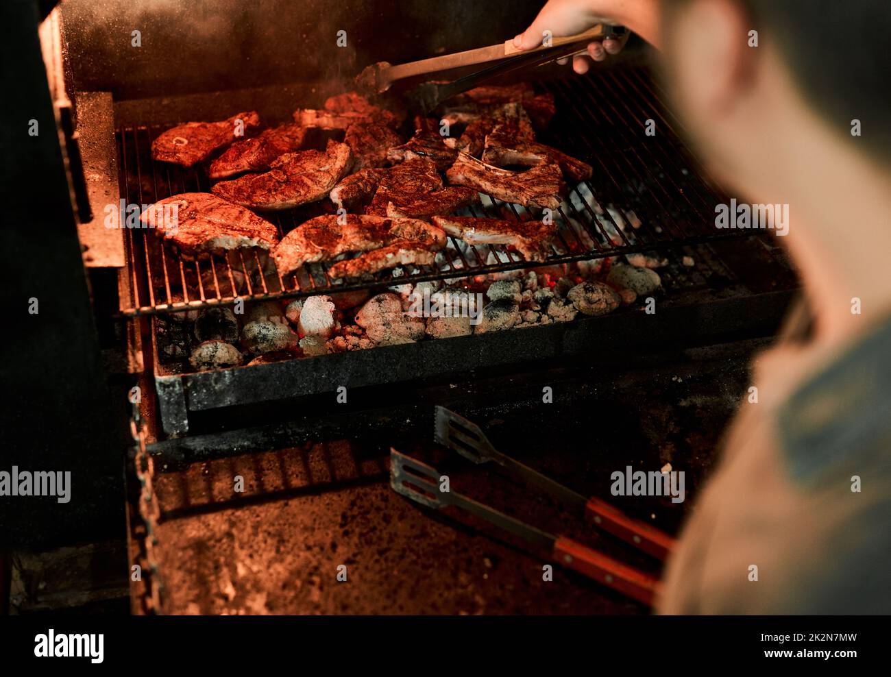 Mantenere la calma e grigliare. Primo piano di un uomo irriconoscibile grigliare carne mentre si fa un barbecue. Foto Stock