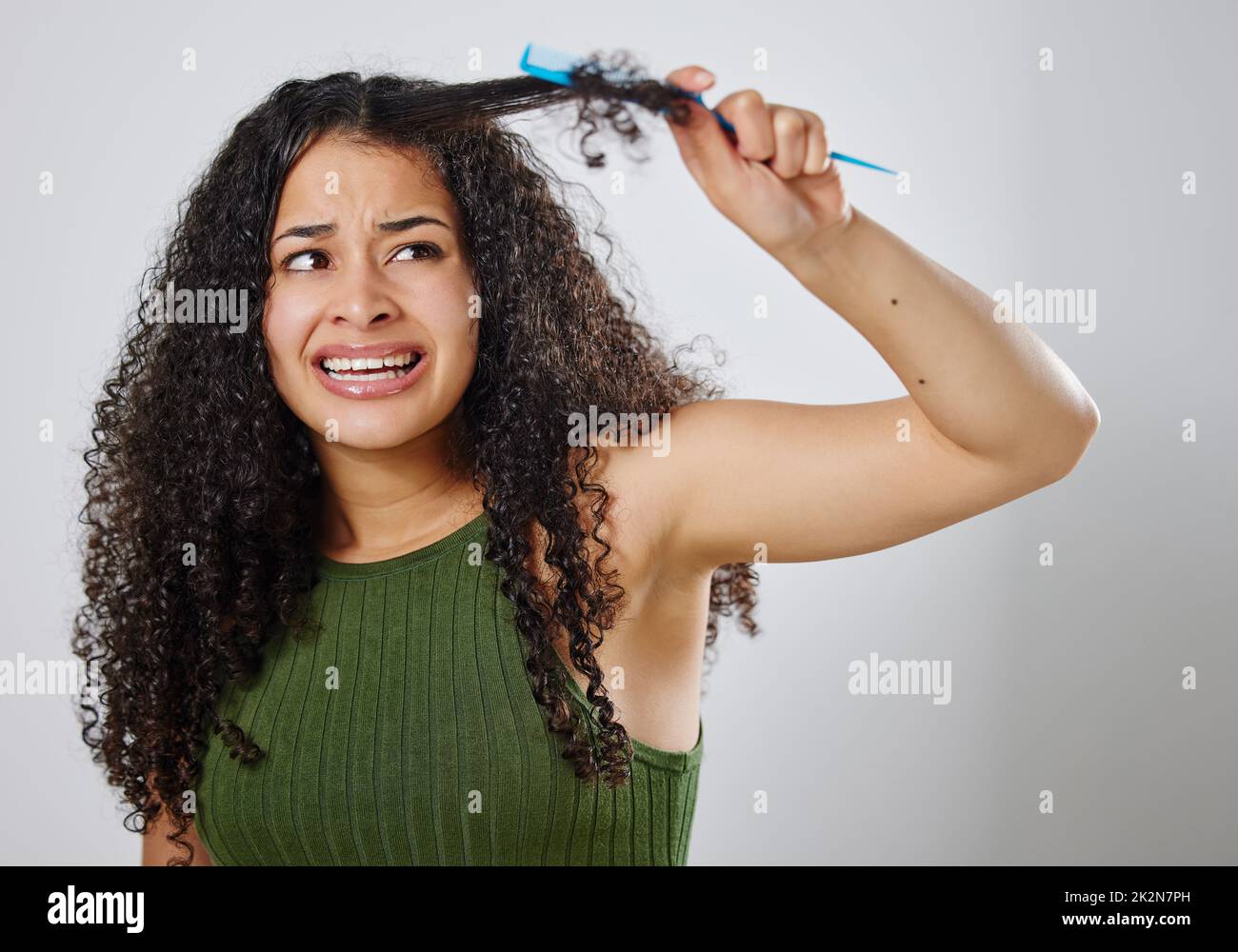 Vorrei che ci fosse un modo più facile per dispettirmi i capelli. Scatto di una donna accigliata mentre pettina i capelli su uno sfondo grigio. Foto Stock