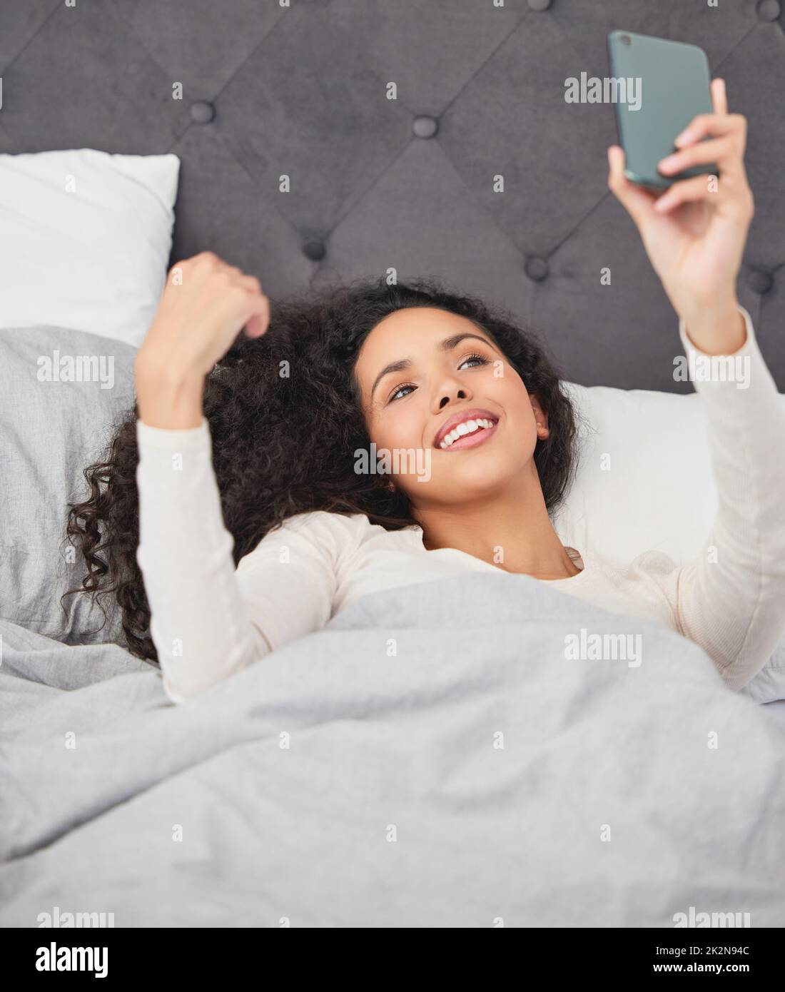 La mattina è meravigliosa. Scatto di una giovane donna che si stendeva a letto e usando il suo cellulare al mattino. Foto Stock