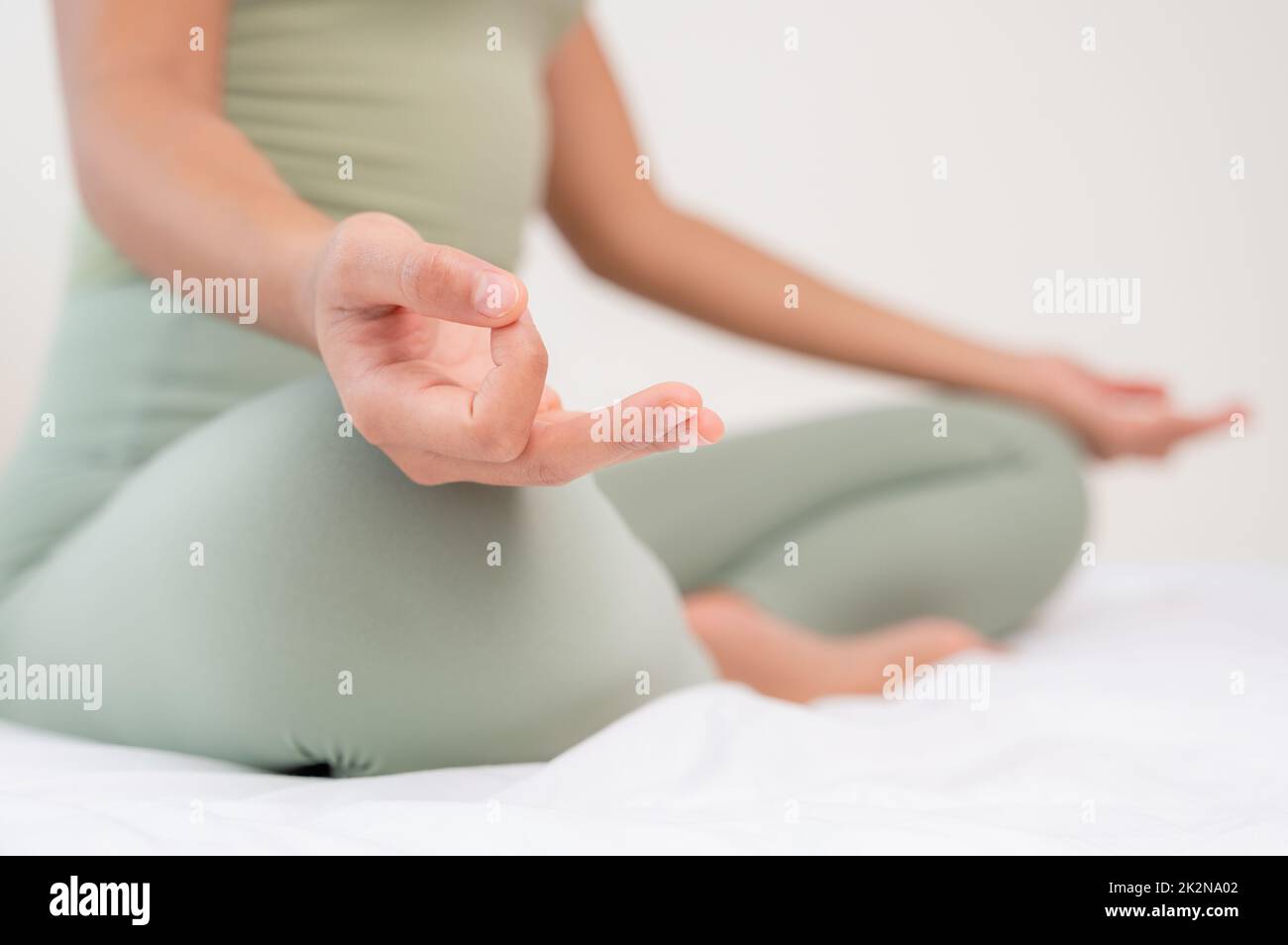 Donna che pratica la meditazione sul letto. Fare yoga respirando con Ardha Padmasana esercizio. Foto Stock