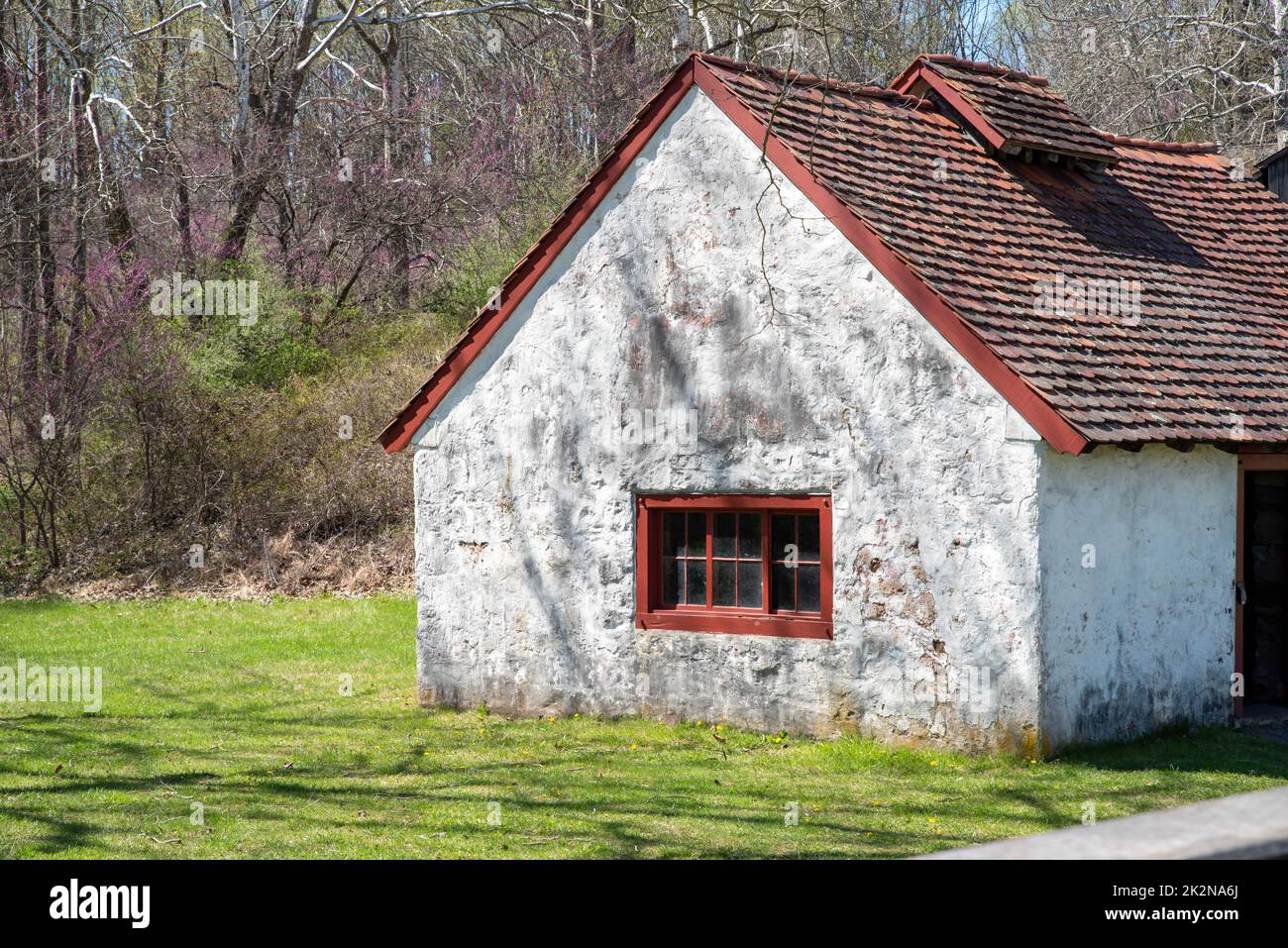 Vista laterale di un cottage in pietra bianca con antica finestra rossa in paesaggio rurale Foto Stock