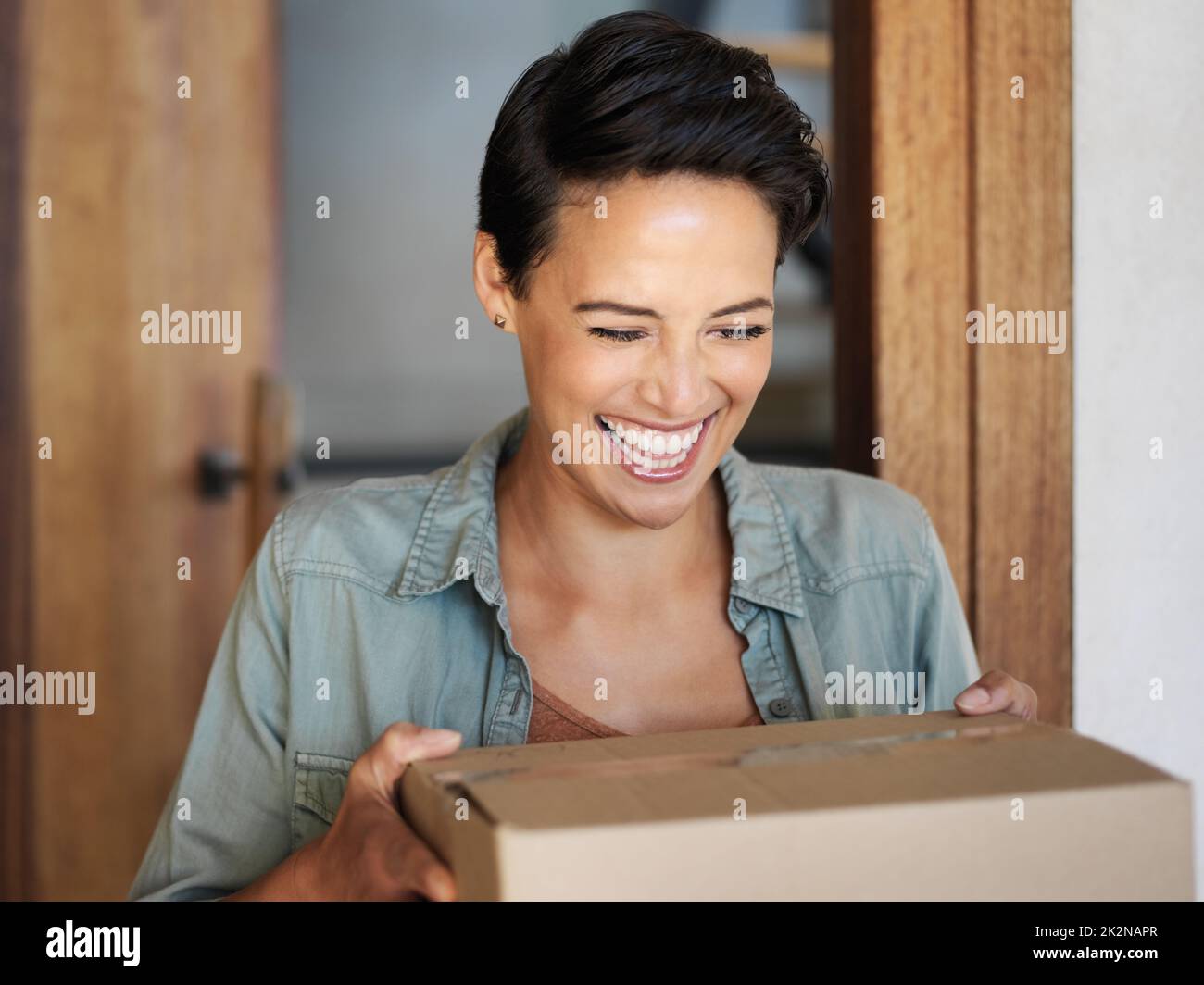 Consegna puntualmente. Scatto di una giovane donna sorridente in piedi alla sua porta di fronte ricevendo un pacco da un corriere. Foto Stock