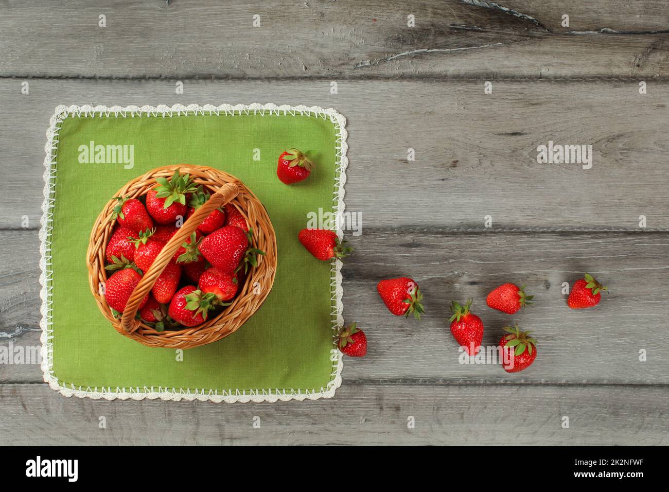 Il piano portapaziente foto, cesto di fragole , alcuni di loro versato sulla tovaglia verde e grigio scrivania in legno. Foto Stock