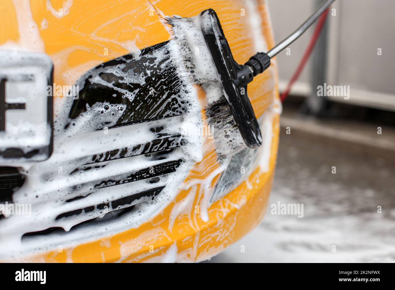 Giallo auto anteriore lavato in self service autolavaggi, bianco shampoo schiuma in contrasto con il nero maschera frontale e spazzola. Foto Stock