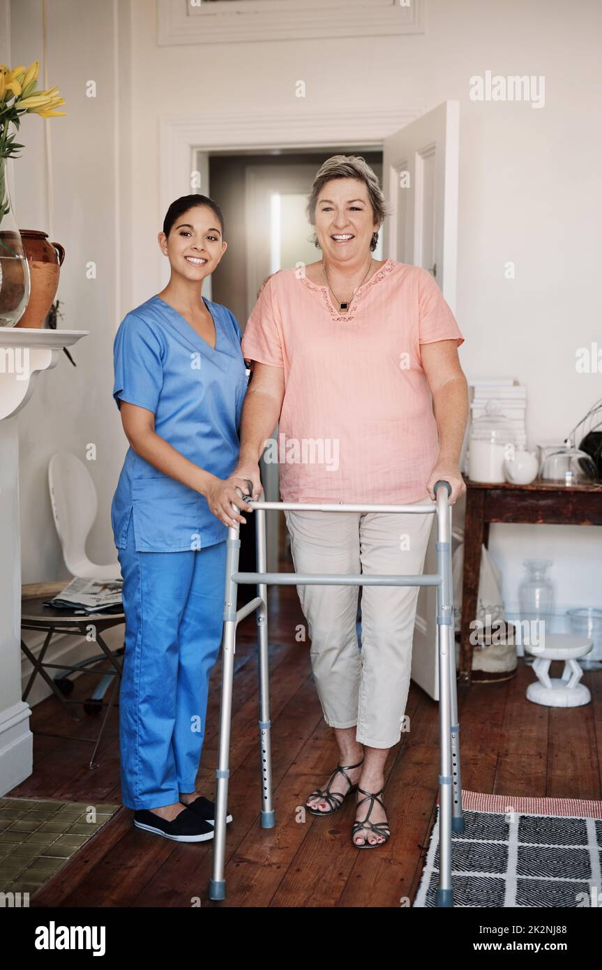 Imparare a camminare di nuovo. Scatto completo di una giovane caregiver femminile attraente che assiste un paziente anziano con un walker in una casa di cura. Foto Stock