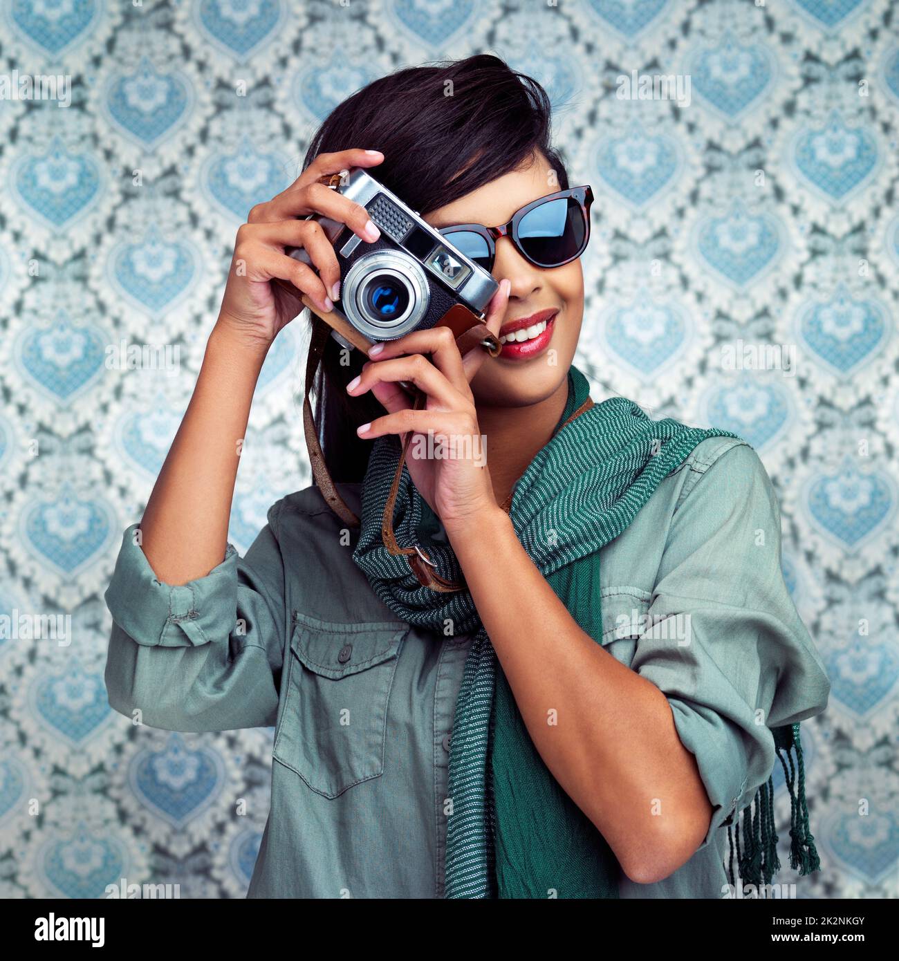 Sorridi per la fotocamera. Scatto di una giovane donna in posa con una macchina fotografica su uno sfondo a motivi geometrici. Foto Stock