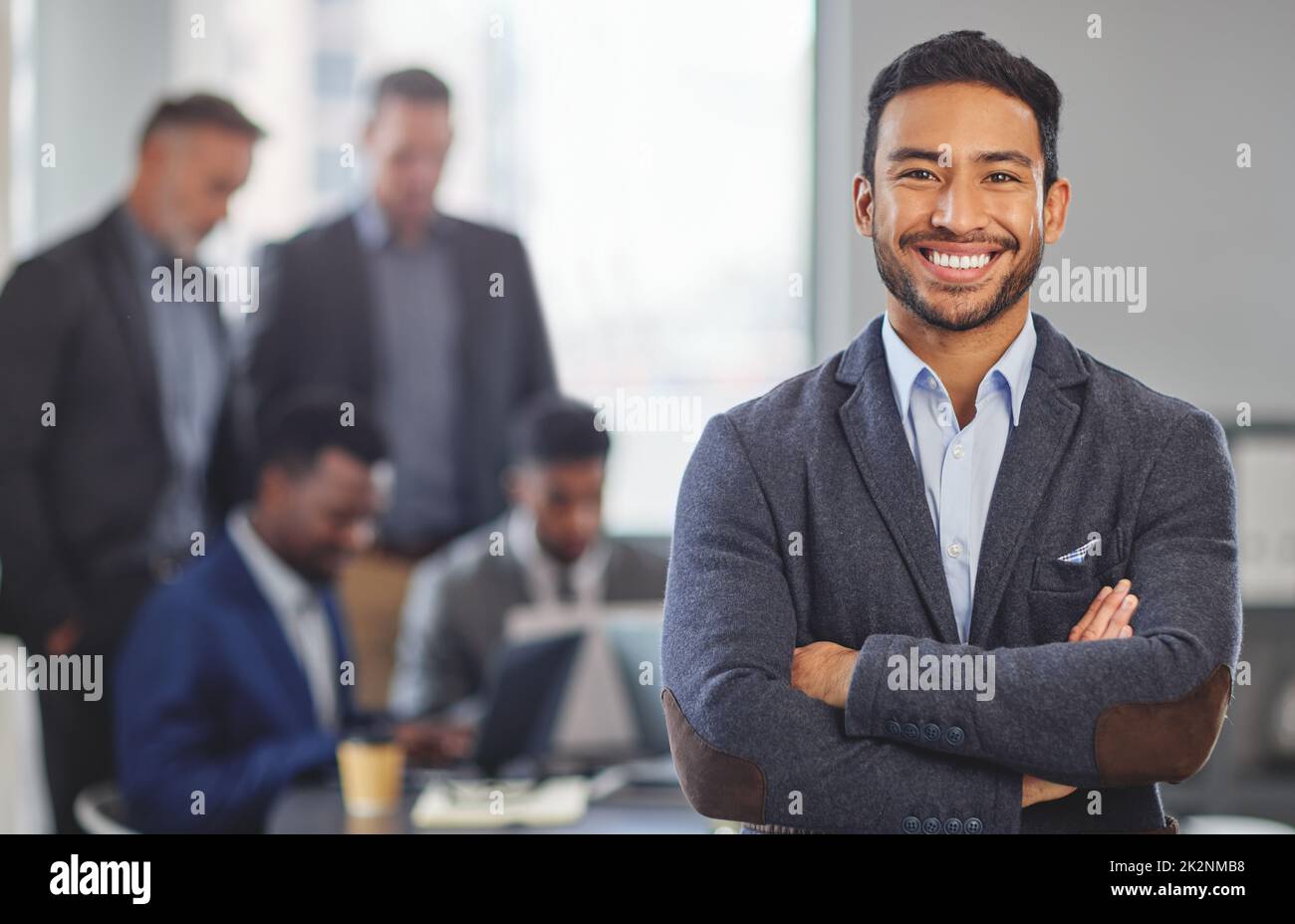 Io chiamo i miei scatti. Ritratto di un giovane uomo d'affari in ufficio in piedi davanti ai suoi colleghi che hanno un incontro in background. Foto Stock