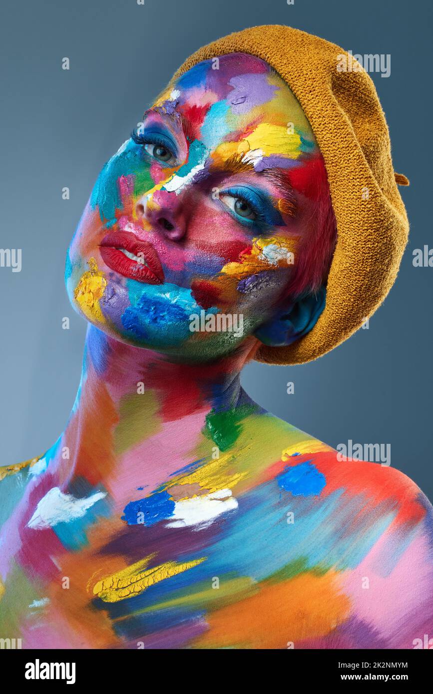 La vita è circa usando l'intera scatola dei pastelli. Studio girato di una giovane donna in posa con vernice multicolore sul suo viso e un cappello francese sulla sua testa. Foto Stock