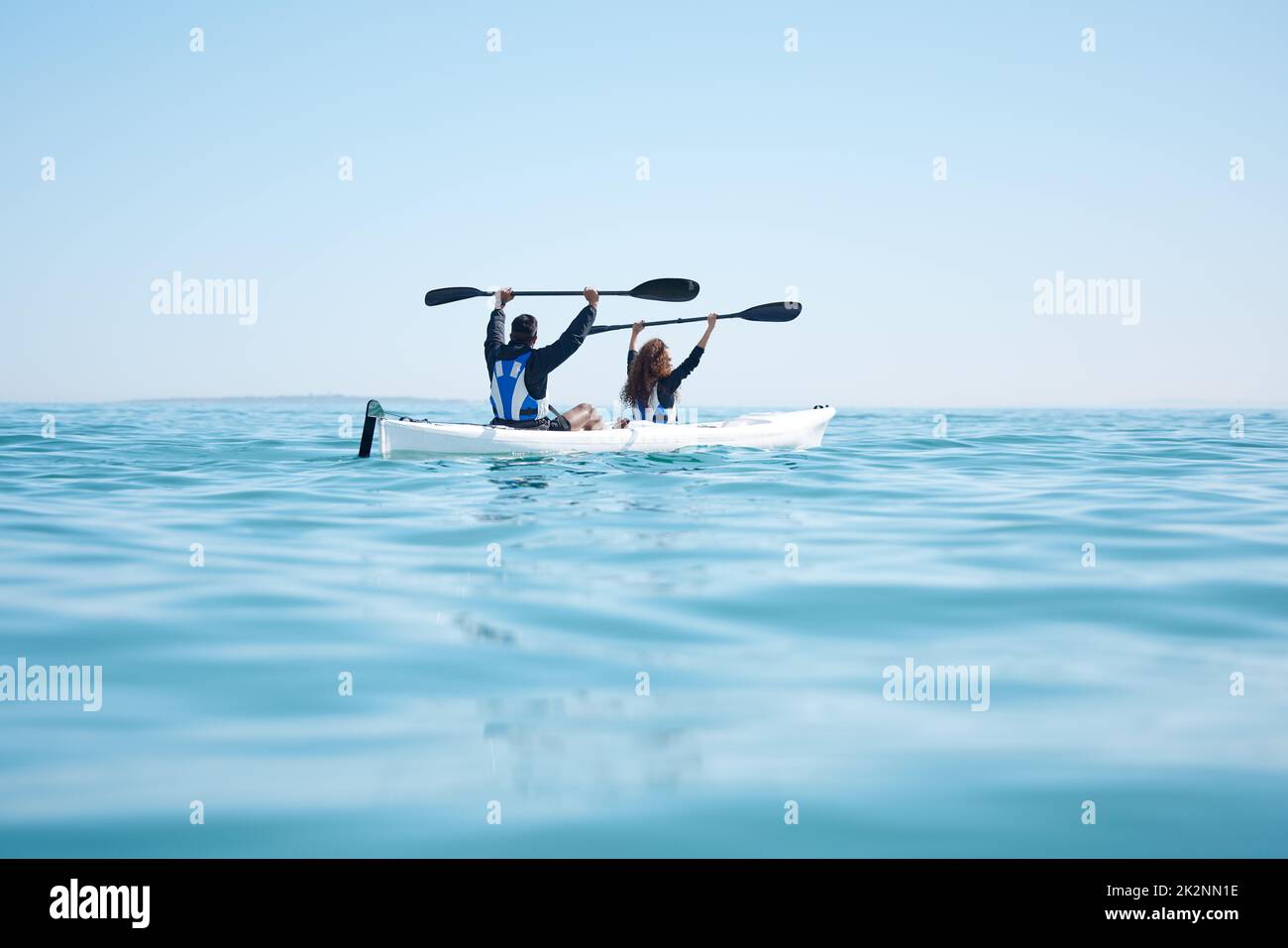 Segnalazione di arresto. Vista posteriore di una giovane coppia che alza i remi mentre si kayak insieme in un lago. Foto Stock