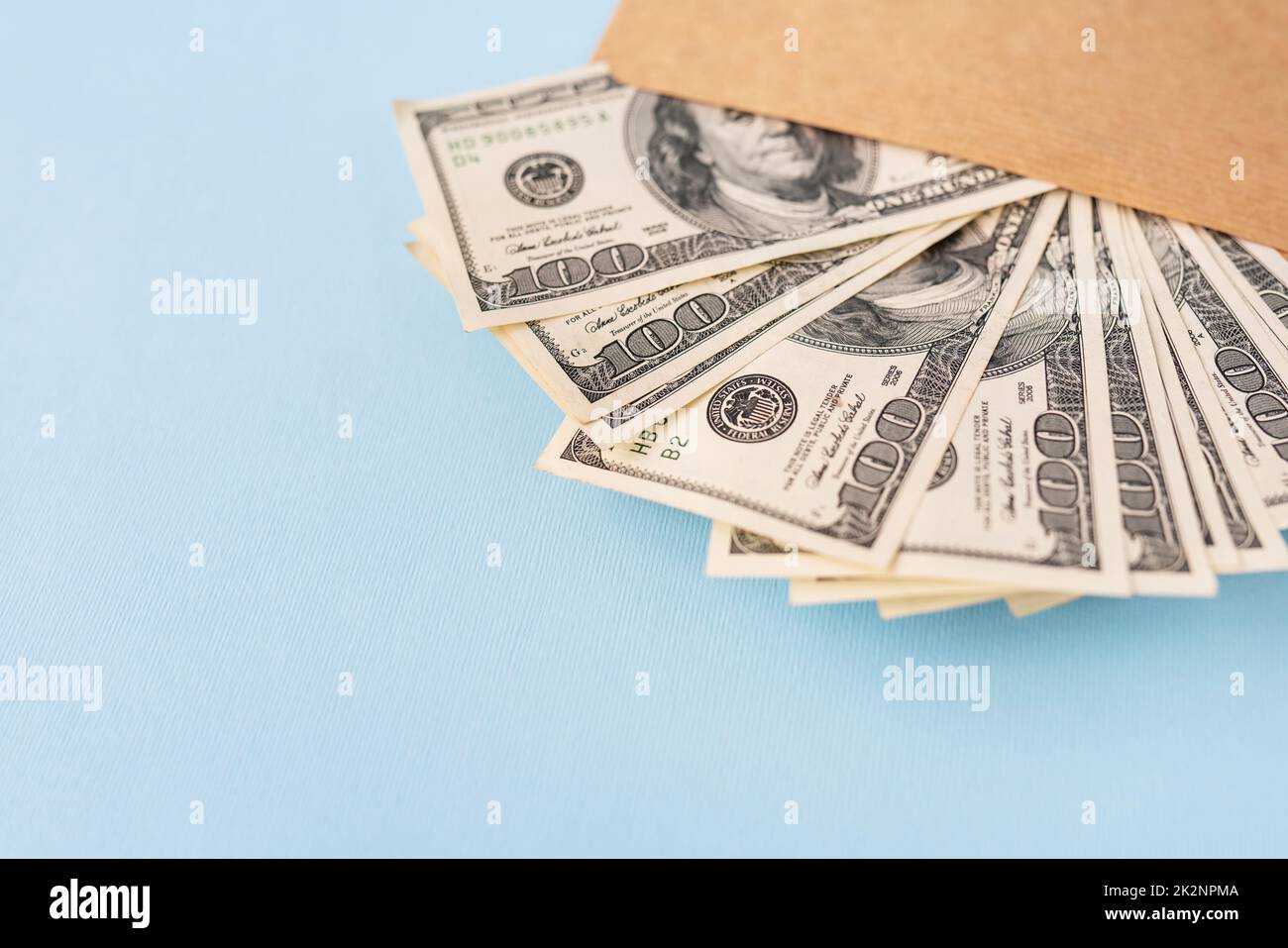 Stash di soldi nelle fatture del dollaro che escono da una busta su uno sfondo blu. Il concetto di stipendio, tangente, prestito, debito, vittoria. Foto Stock