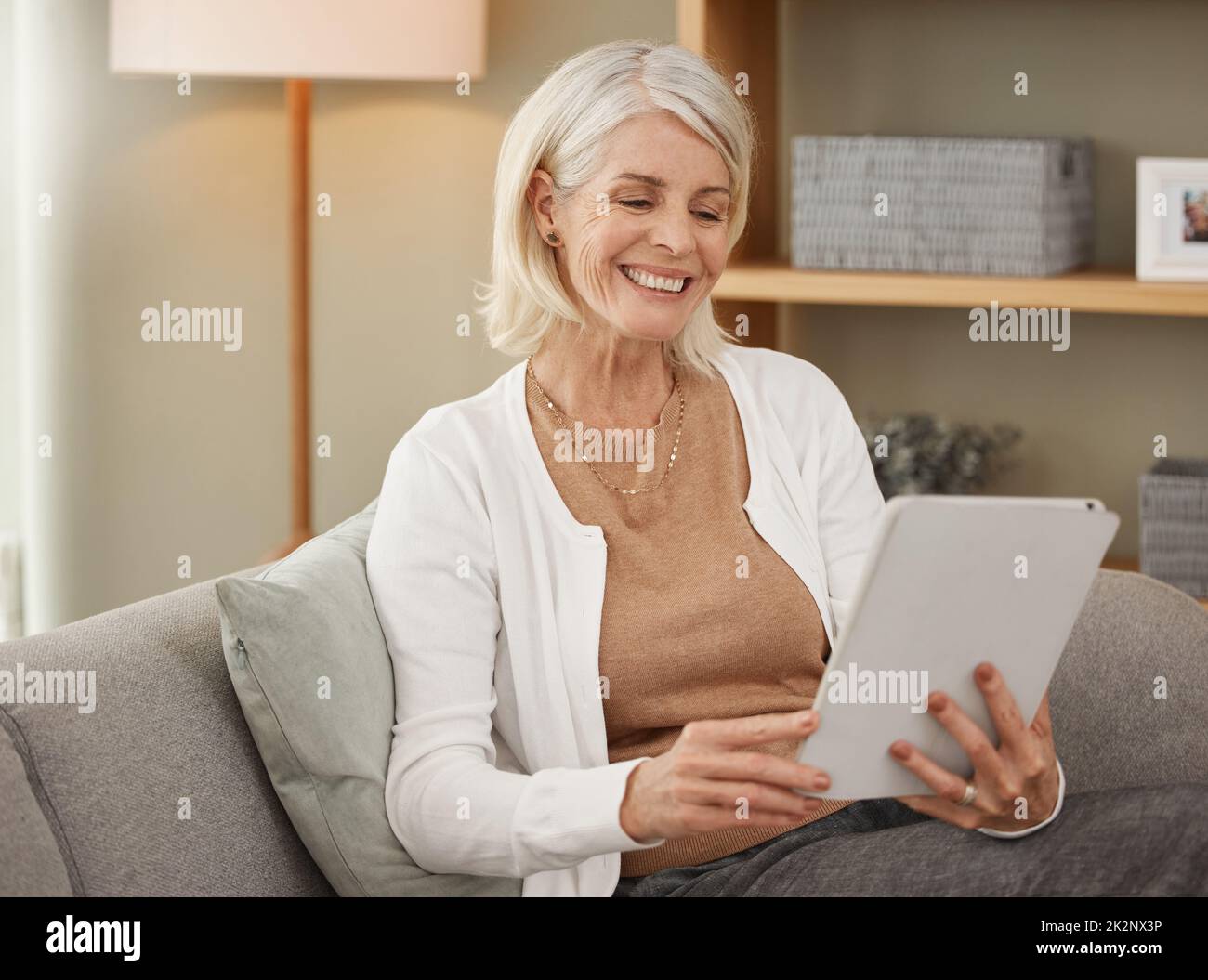 Il relax inizia adesso. Scatto di una donna matura utilizzando un tablet digitale sul divano di casa. Foto Stock