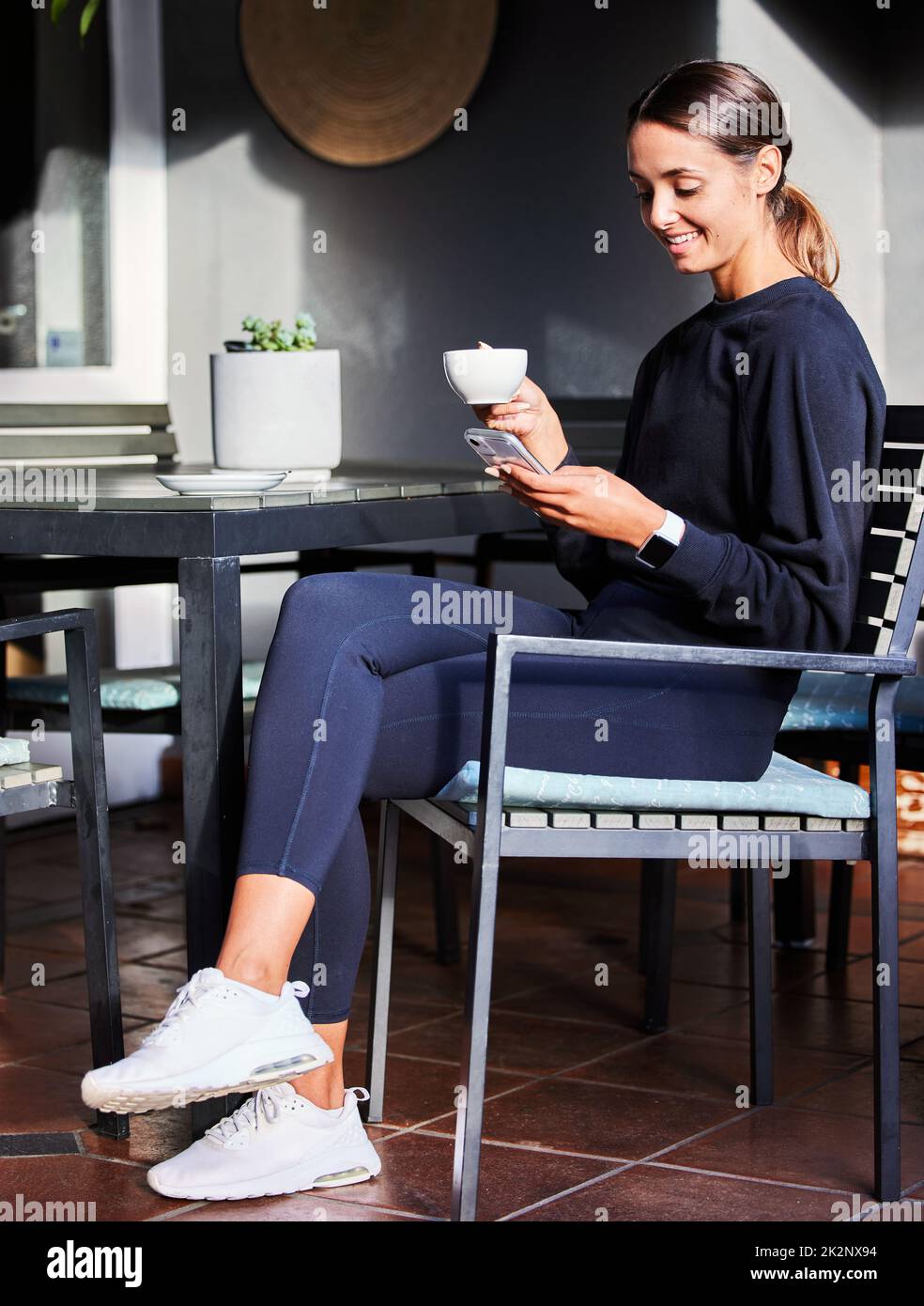 Pausa caffè. Shot di una donna che usa il suo cellulare mentre si siede all'esterno con una tazza di caffè. Foto Stock