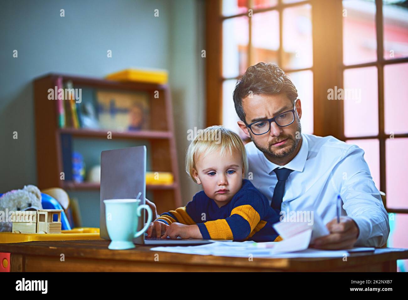 Si occupa del suo bambino e del suo business allo stesso tempo. Sparato di un singolo padre che passa attraverso il lavoro di ufficio a casa. Foto Stock