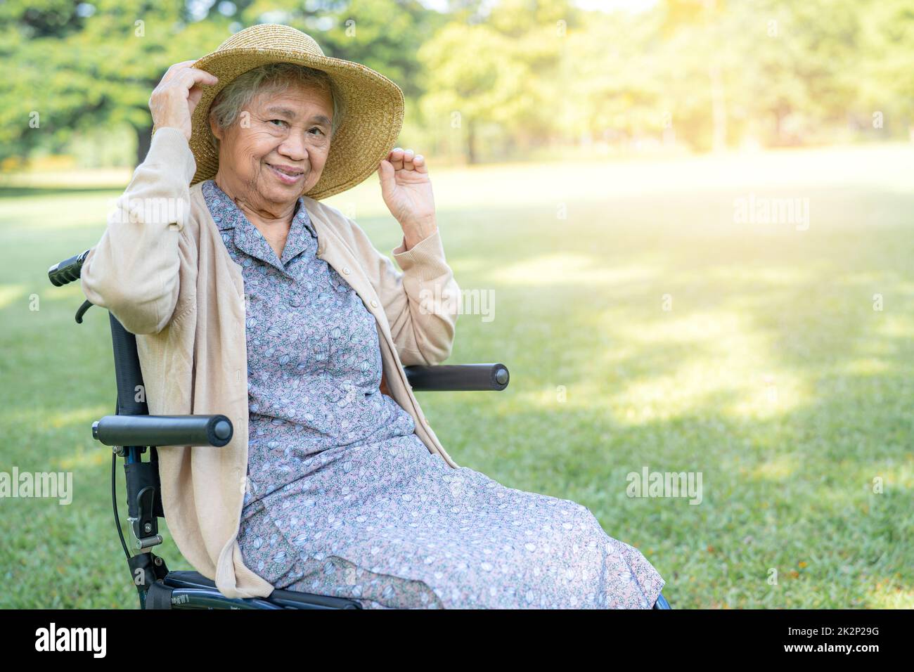Una donna anziana viaggiatore con cappello di paglia seduto su sedia a rotelle nel parco. Foto Stock