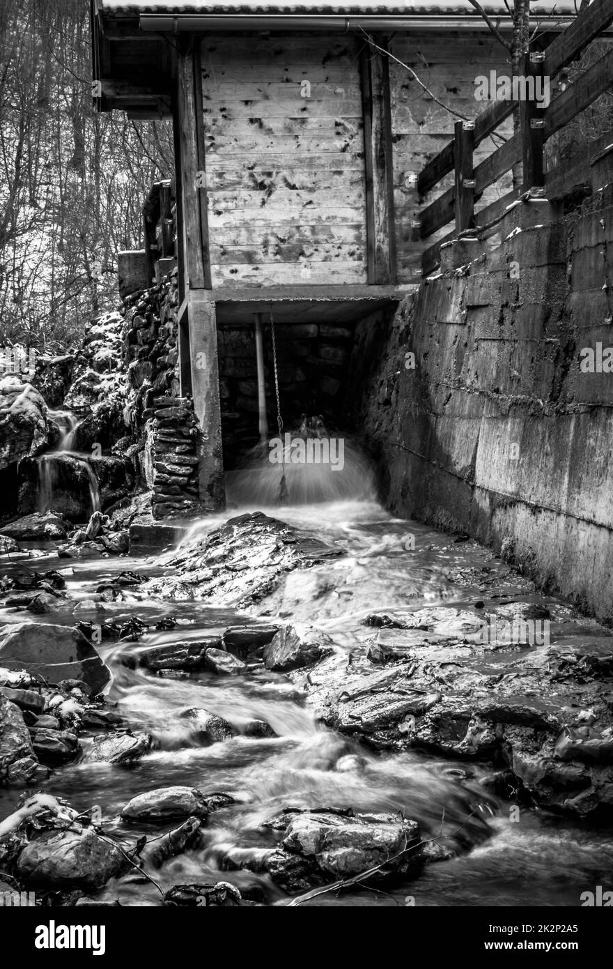 Scala di grigi verticale dell'acqua fluviale che scorre dal tunnel Foto Stock