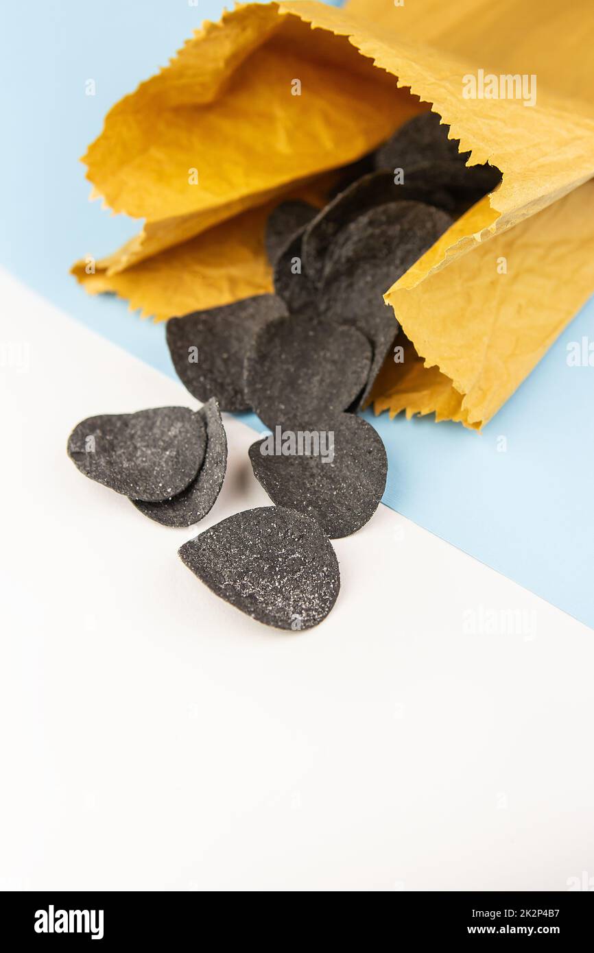 Messa a fuoco selettiva. Macrofoni in una borsa artigianale. Spezie e sale su patatine nere. Patatine nere con spezie su un piatto, seppie inchiostro alimentare. Foto Stock