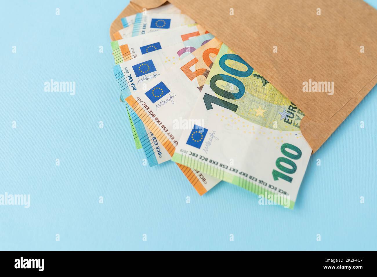 Una cache di moneta in euro, in banconote di 100 tagli, che esce da una busta su sfondo blu. Il concetto di stipendio, tangente, prestito, debito, vittoria. Foto Stock