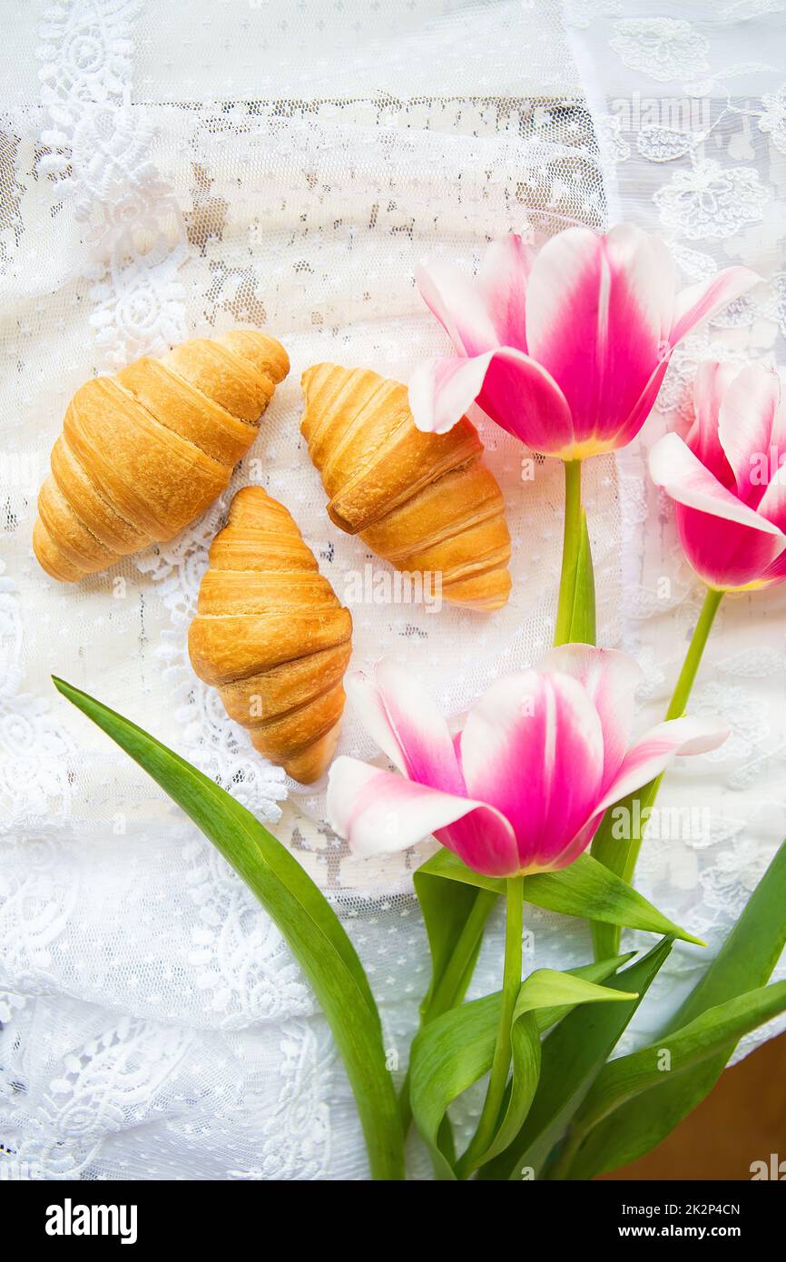 Tre croissant e rosa luminoso tulipani sulla tovaglia di pizzo Foto Stock