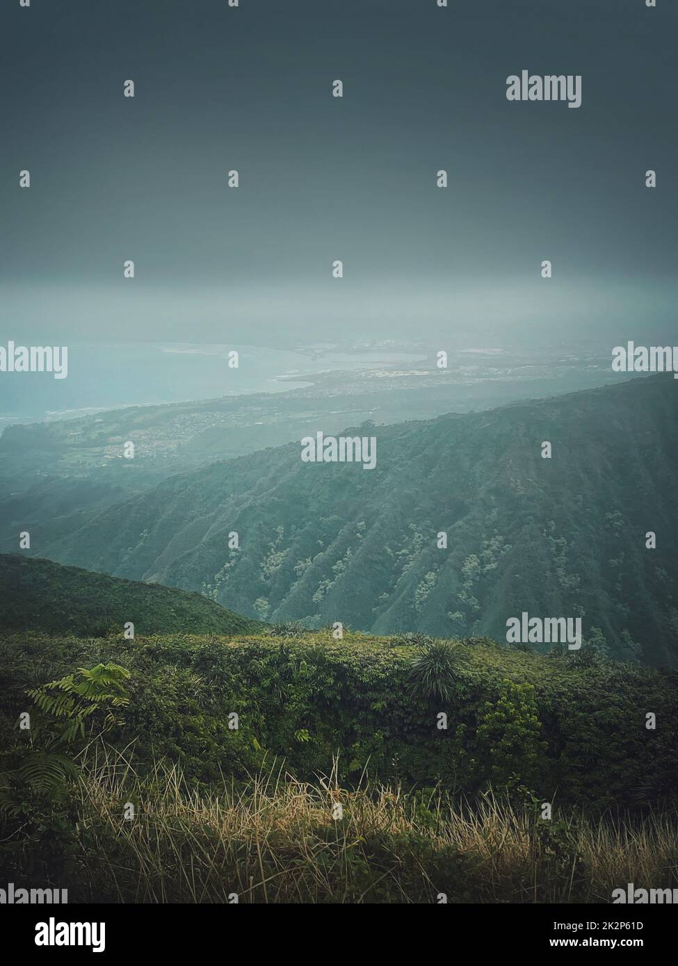 Vista panoramica dalla cima delle montagne alla costa dell'oceano alle Hawaii, isola di Oahu. Moody paesaggio escursionistico con nebbia, verdi colline all'orizzonte e nuvole tempestose sulla baia Foto Stock