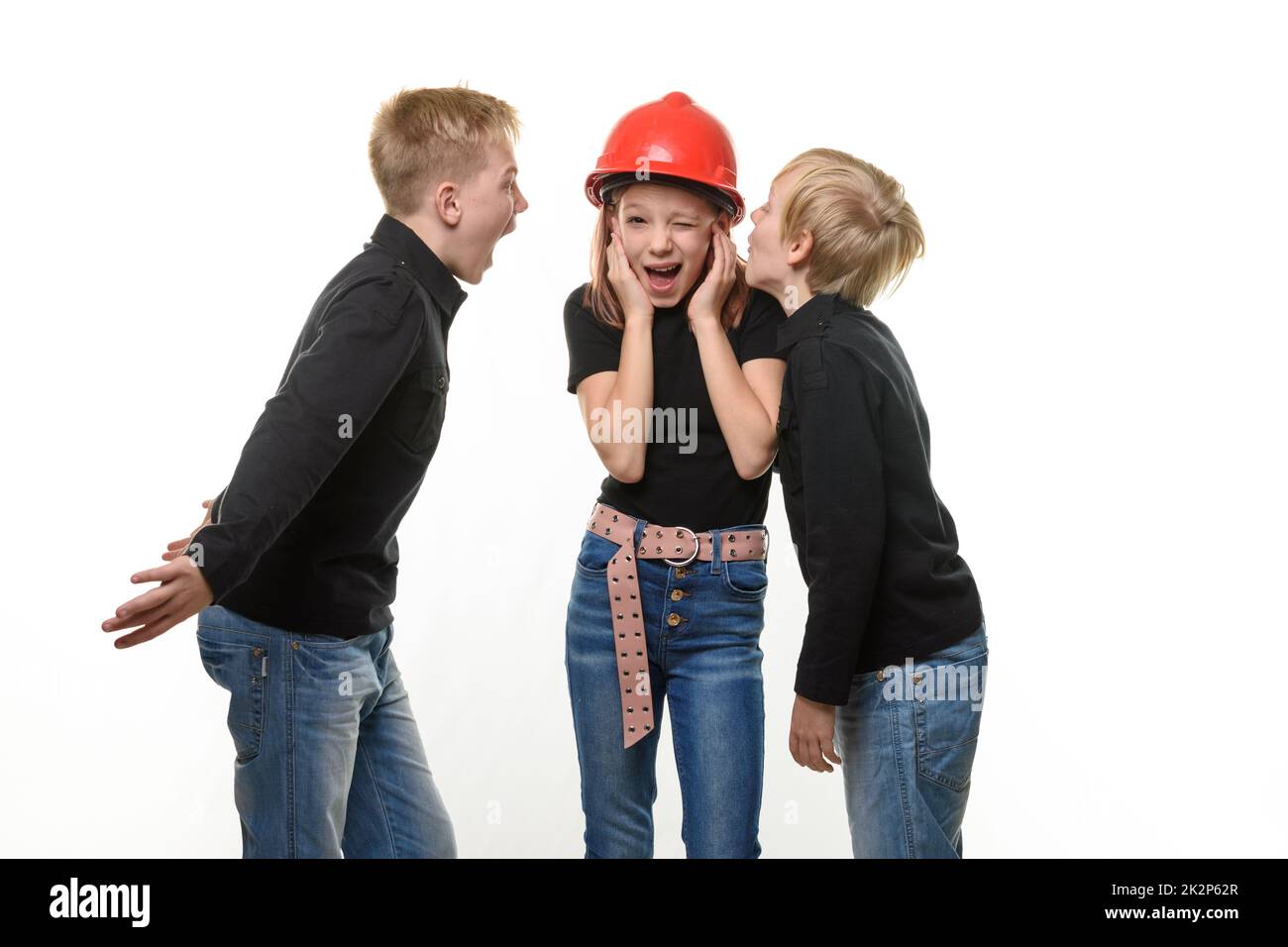 Due ragazzi gridano ad una ragazza, la ragazza è in piedi in un casco in un elmetto e tappò le orecchie, isolato su uno sfondo bianco Foto Stock