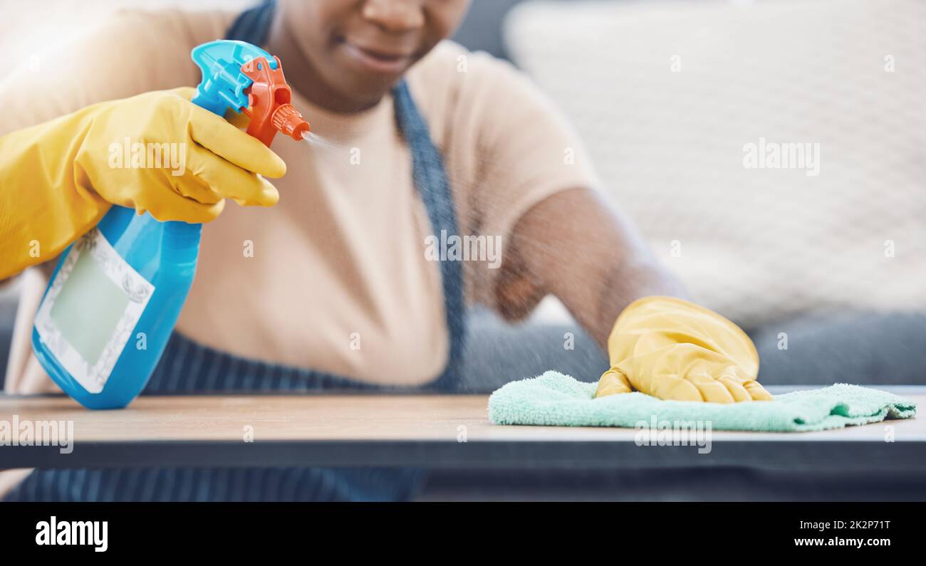 Donna con detergente per pulire, spruzzare e pulire il tavolo, in ufficio o in soggiorno a casa. Donna nera nel lavoro domestico, utilizzare panno e detergente liquido, su Foto Stock