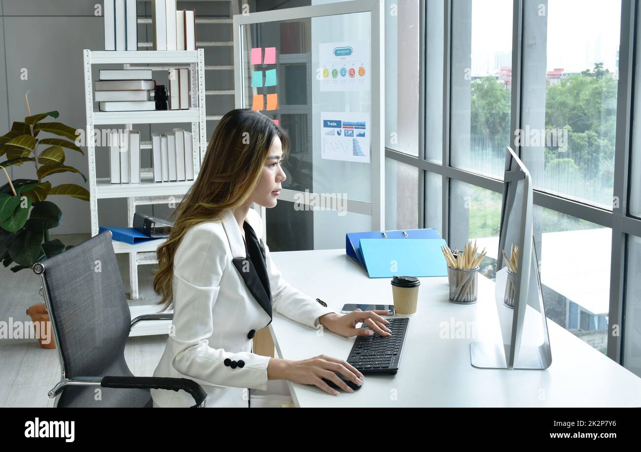 Bella donna asiatica d'affari che guarda lo schermo del computer portatile a lavorare in ufficio Foto Stock