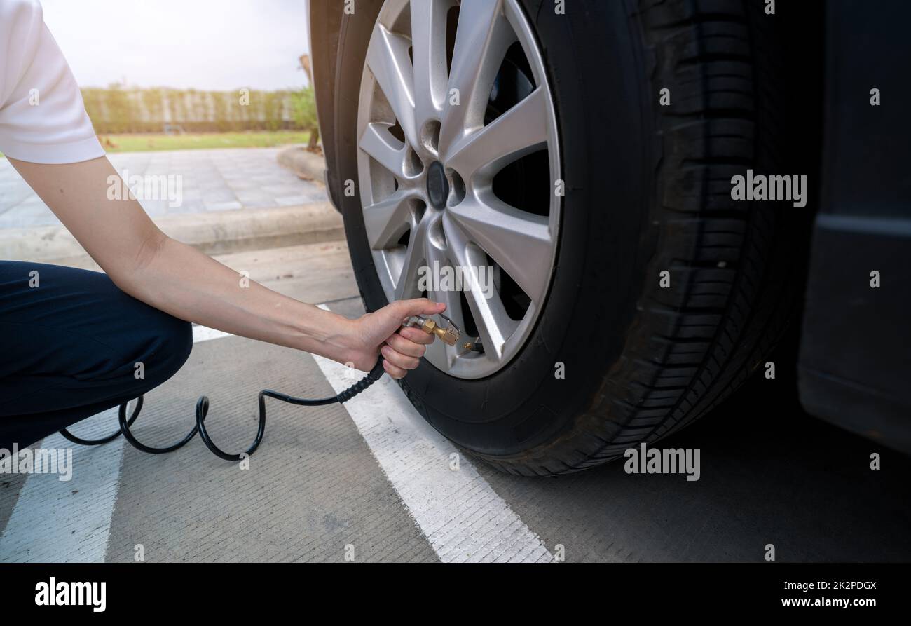 Donna gonfia il pneumatico. Donna che controlla la pressione degli pneumatici e che pompa aria nello pneumatico della ruota dell'automobile. Servizio di manutenzione dell'auto per la sicurezza prima del viaggio. Punto di gonfiaggio pneumatico. Riempimento di aria nello pneumatico dell'auto Foto Stock