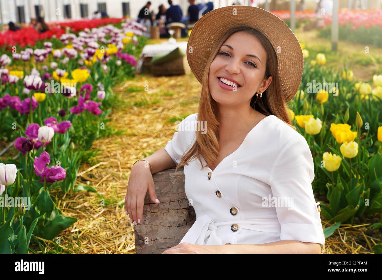 Ritratto di sorridente ragazza seduta rilassato tra i campi di tulipani in primavera. Guardando la fotocamera. Foto Stock