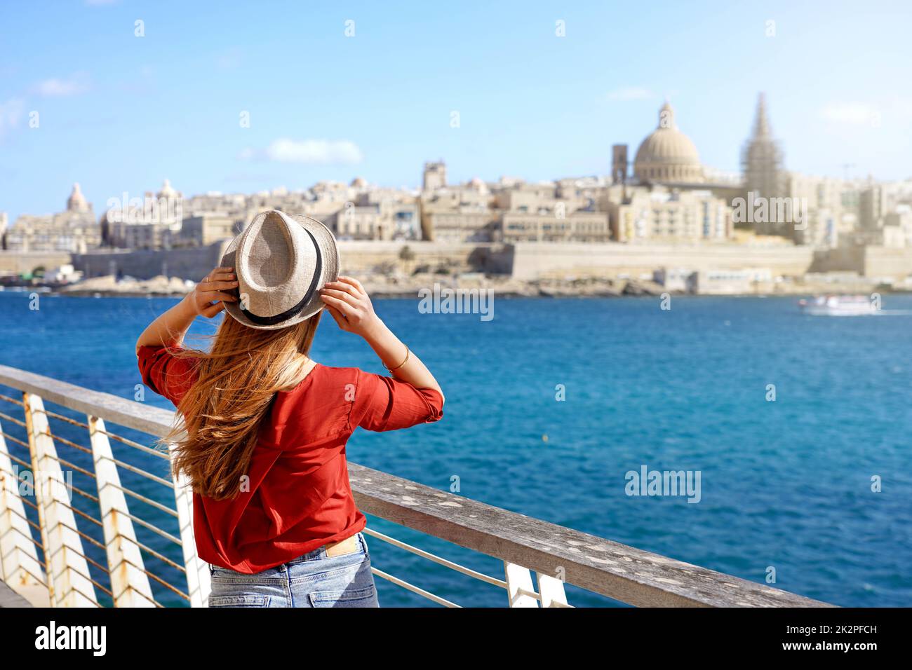 Turismo in Europa. Ragazza viaggiatore che tiene cappello a piedi lungo la passeggiata di Malta con la Valletta paesaggio urbano sullo sfondo. Foto Stock