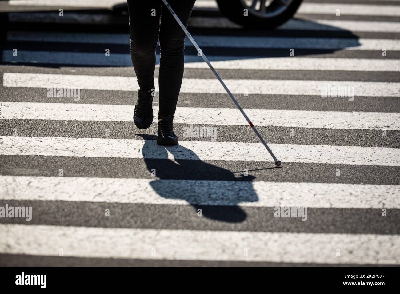 Donna cieca che cammina per le strade della città, utilizzando la sua canna bianca per navigare meglio lo spazio urbano e per raggiungere la sua destinazione in modo sicuro Foto Stock