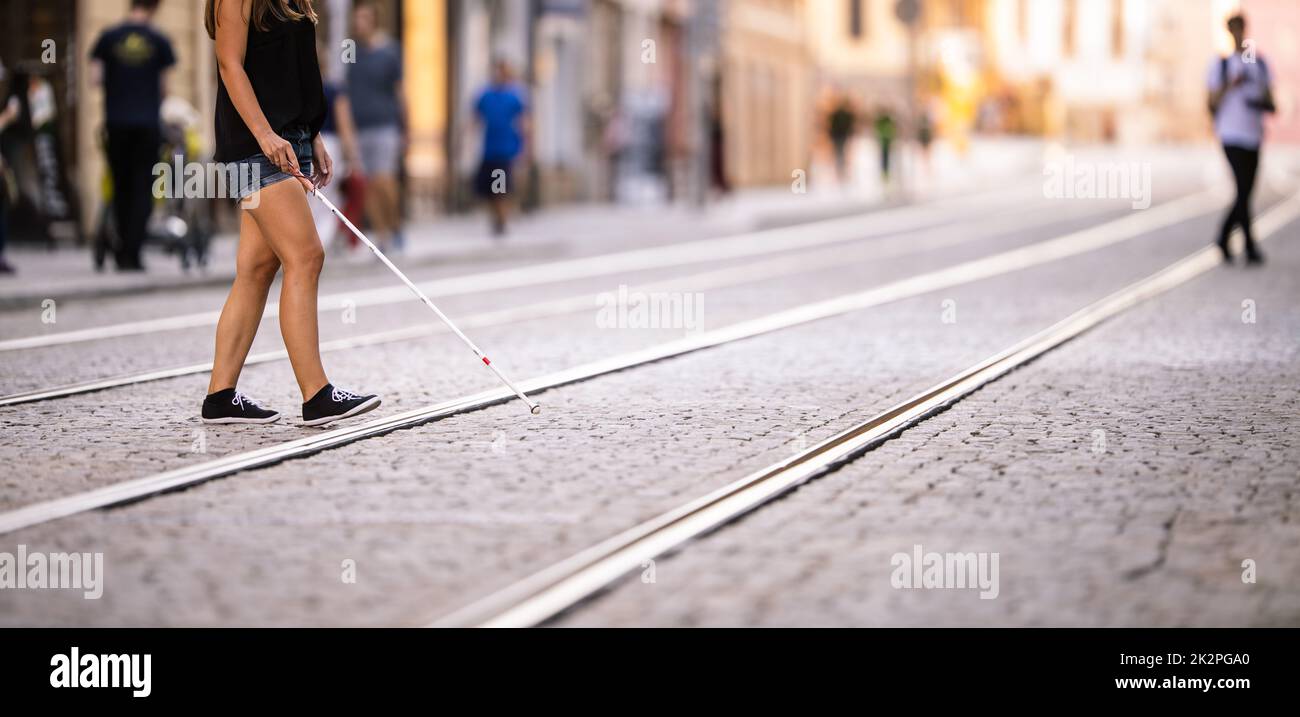 Donna cieca che cammina per le strade della città, utilizzando la sua canna bianca per navigare meglio lo spazio urbano e per raggiungere la sua destinazione in modo sicuro Foto Stock