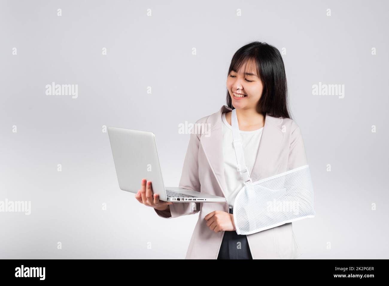 Donna asiatica d'affari sicura sorridente braccio rotto dopo incidente e indossare stecca braccio per il trattamento, ma ancora devono lavorare lei tenere un computer portatile Foto Stock