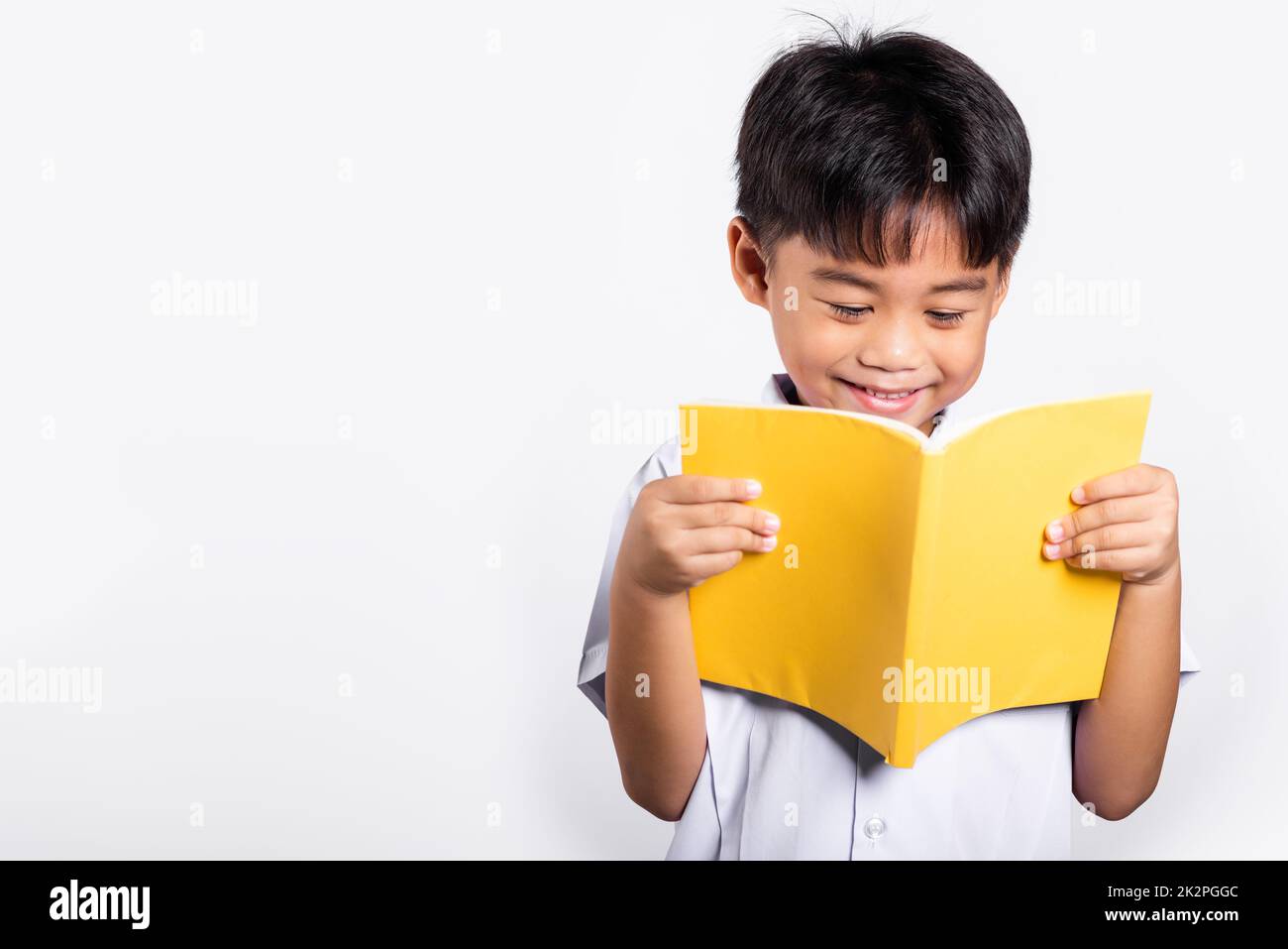 Asian toddler sorriso felice indossando studente thai uniforme pantaloni rossi in piedi tenendo e leggendo un libro Foto Stock