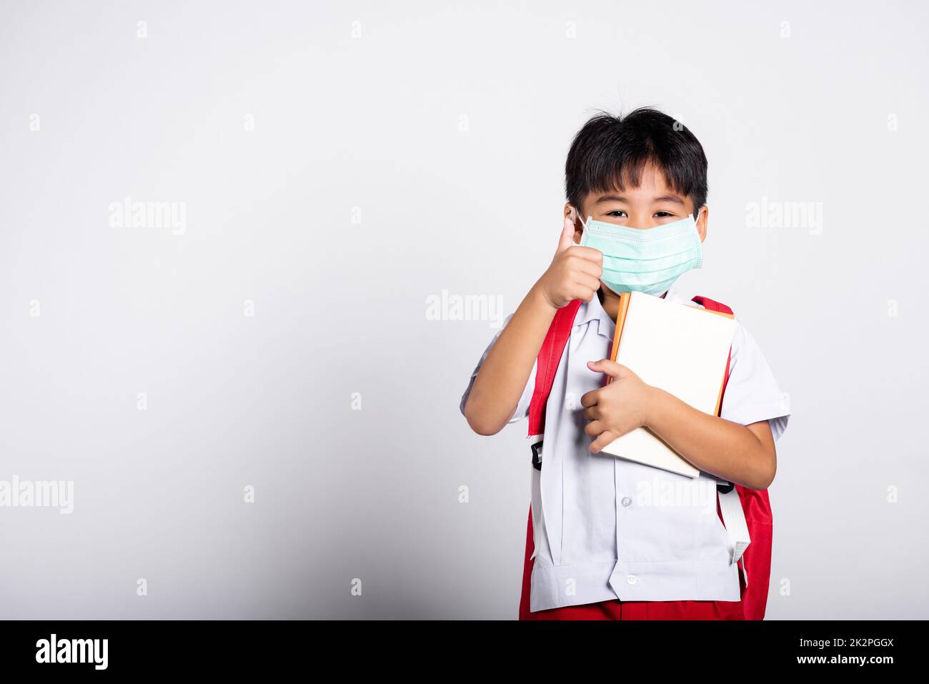 Ragazzo asiatico studente ragazzo con l'uniforme tailandese studente e medico proteggere maschera viso e mostrare pollice fino dito per il bene Foto Stock