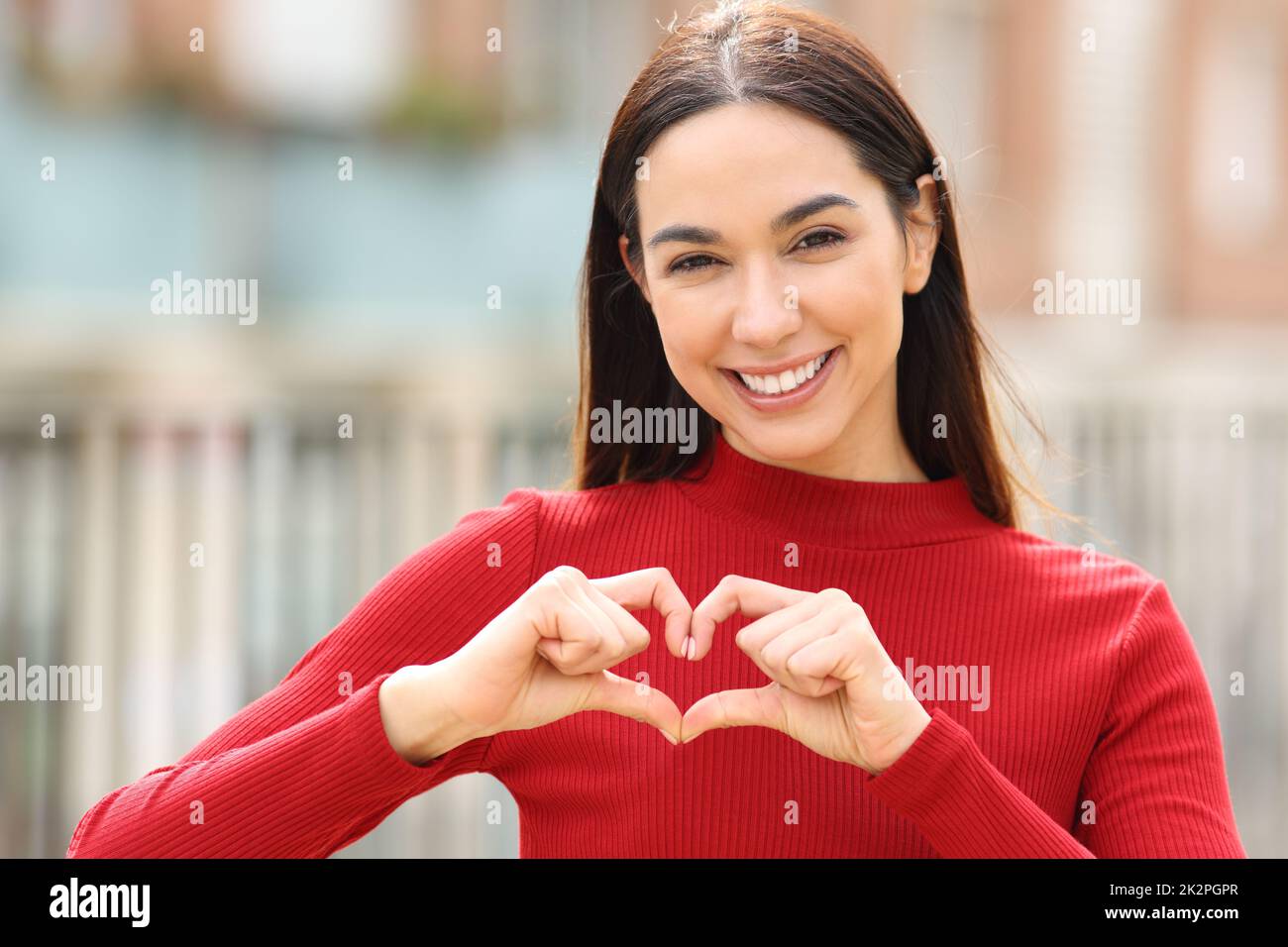 Donna felice che fa la forma del cuore con le mani in strada Foto Stock