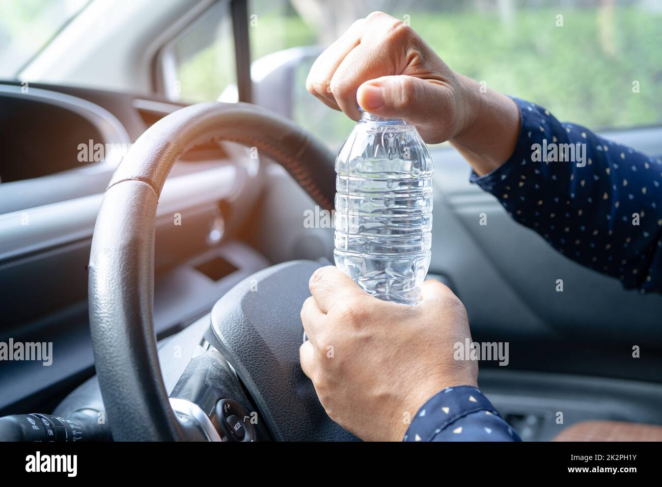 Donna asiatica conducente che tiene una bottiglia per bere acqua mentre guida una macchina. La bottiglia di plastica dell'acqua calda provoca un incendio. Foto Stock