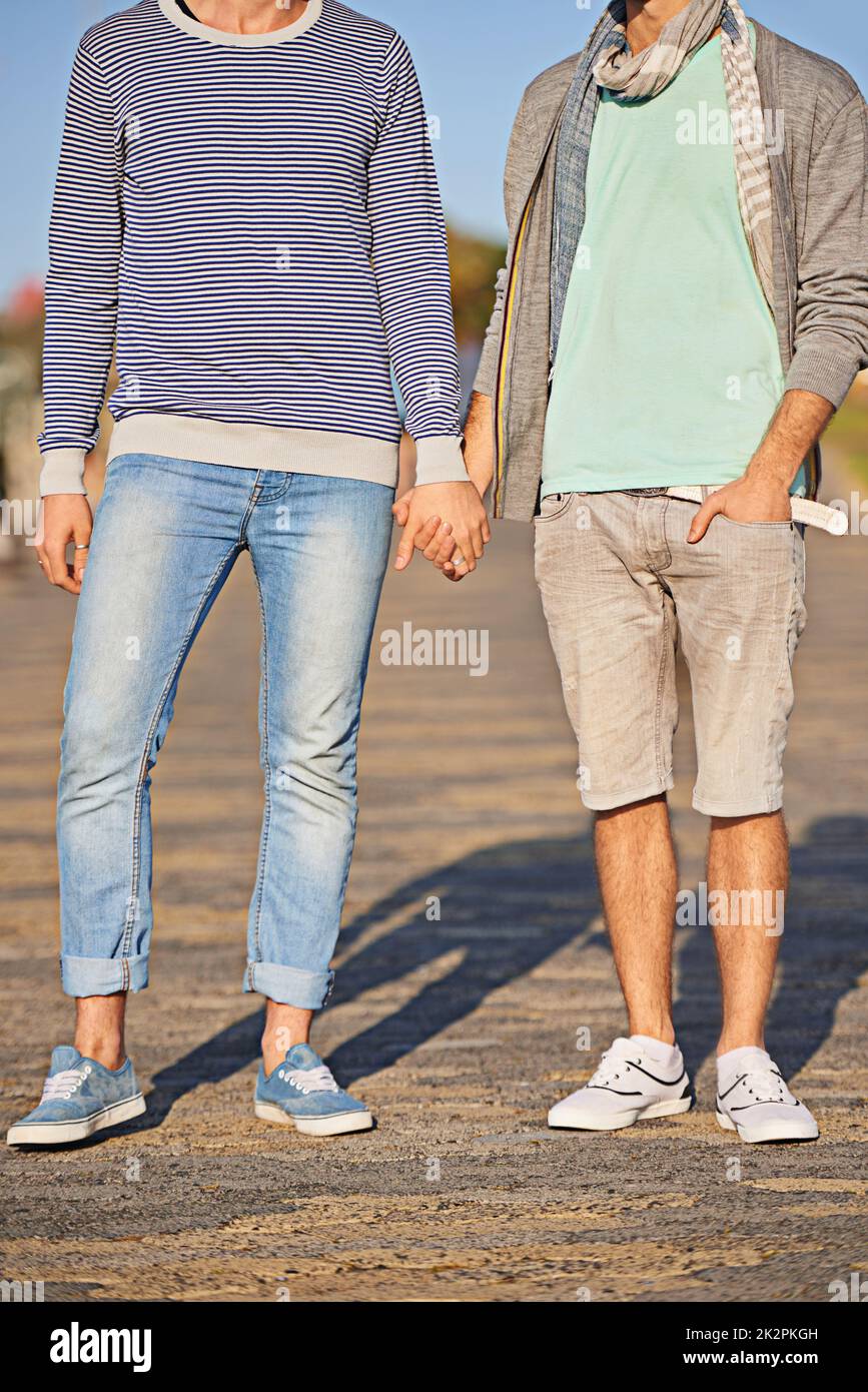 Mano nella mano attraverso la vita. Una giovane coppia gay godendo di una passeggiata sul lungomare insieme. Foto Stock