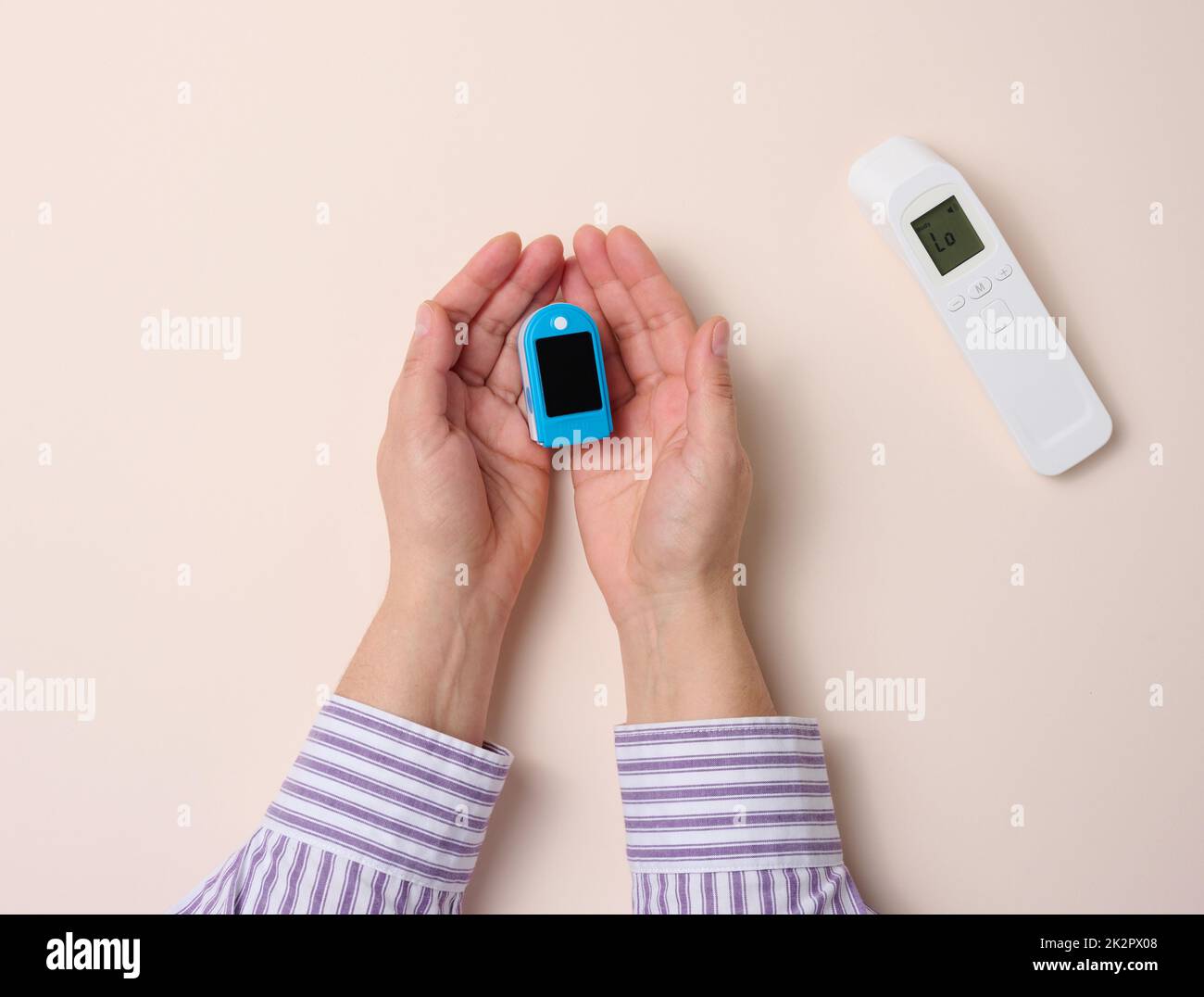 la mano femmina tiene il termometro in plastica senza contatto e l'ossimetro su sfondo beige Foto Stock