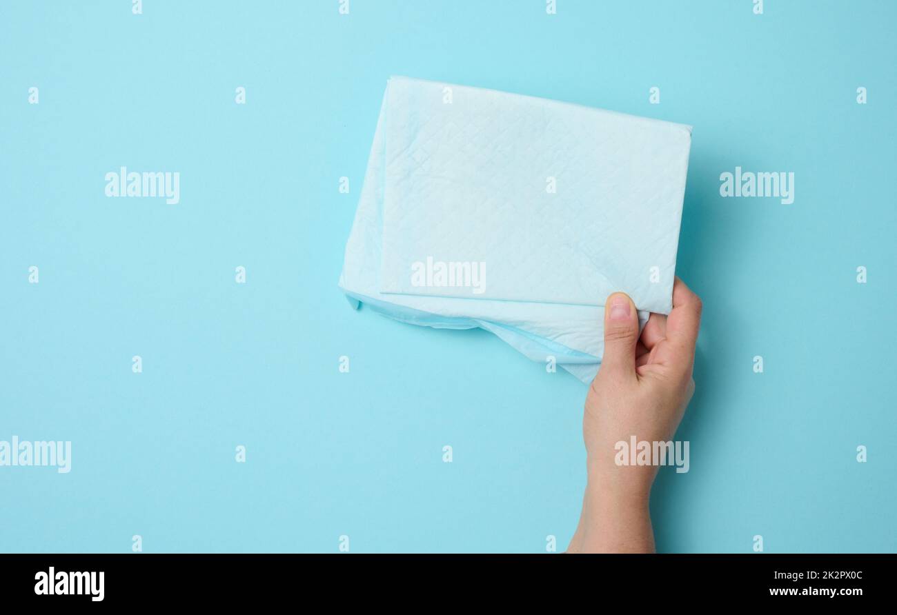 la mano femminile tiene un pannolino medico usa e getta su uno sfondo blu. Prodotto igienico Foto Stock