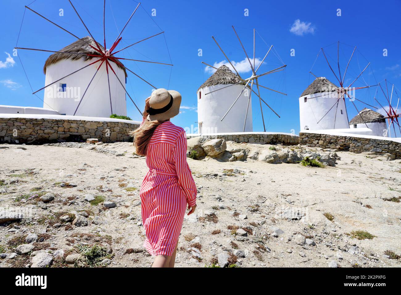 Giovane donna che cammina tra i tradizionali mulini a vento greci sull'isola di Mykonos, Cicladi, Grecia Foto Stock