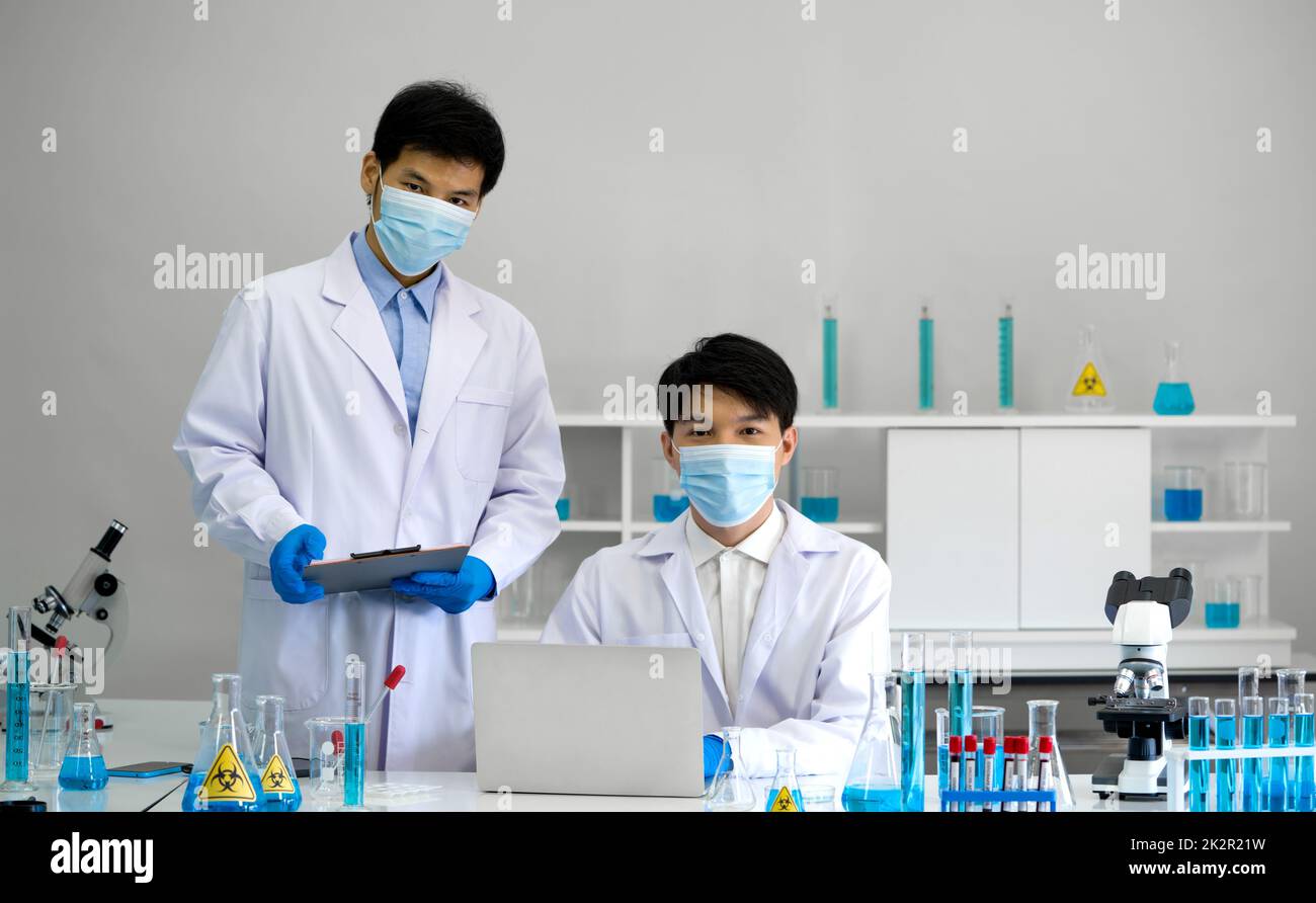 Due scienziati con maschera facciale e abito che lavorano in laboratorio. Processo di test del ceppo Omicron, malattia di Coronavirus 2019. Foto Stock