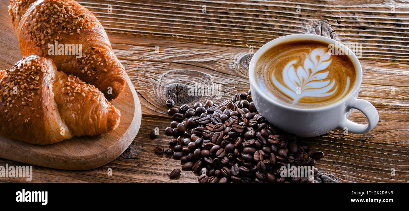 Una tazza di caffè e due croissant su un vecchio tavolo di legno Foto Stock