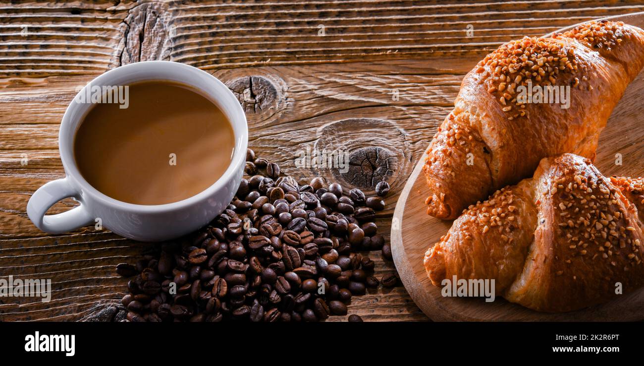 Una tazza di caffè e due croissant su un vecchio tavolo di legno Foto Stock