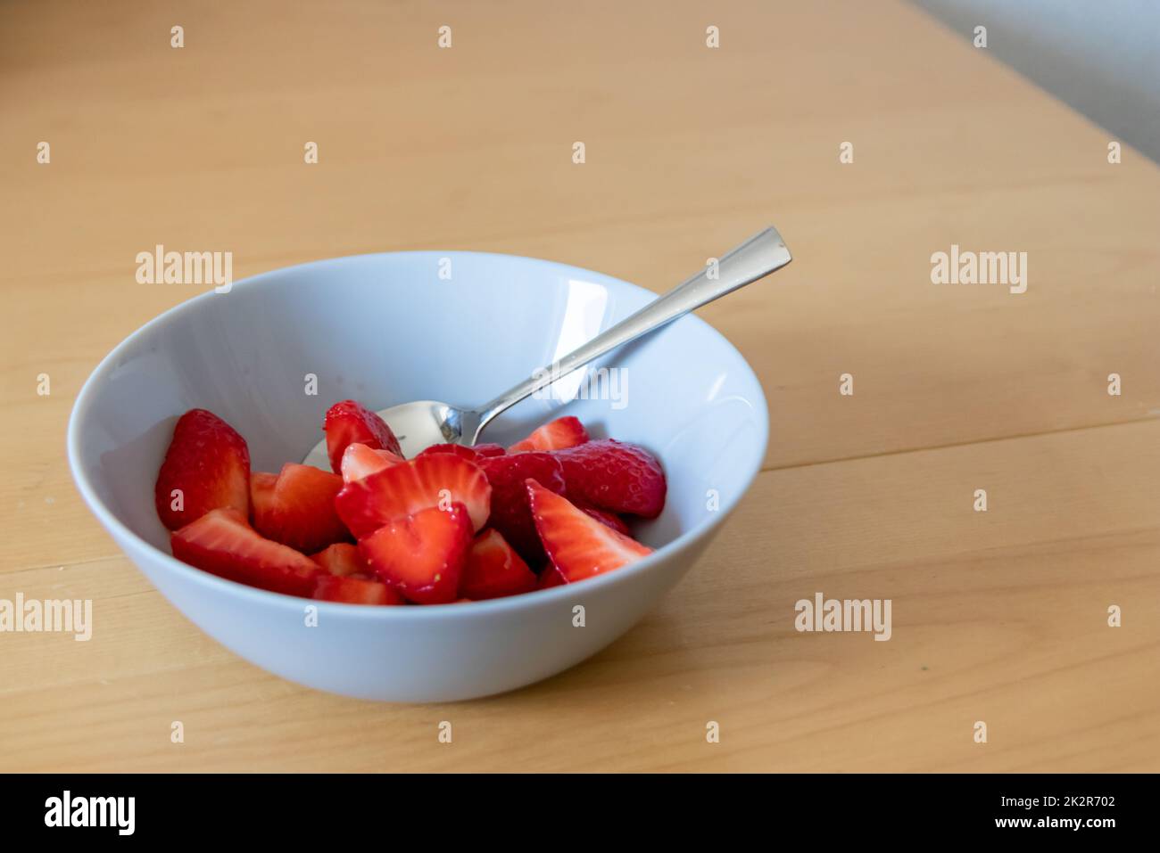 Molte fragole tagliate in ciotola sono pronte a mangiare con cucchiaio d'argento o come delizioso cibo per le dita e uno spuntino sano con frutta rossa e vitamine sul tavolo da cucina in legno per un'alimentazione e una salute sostenibili Foto Stock