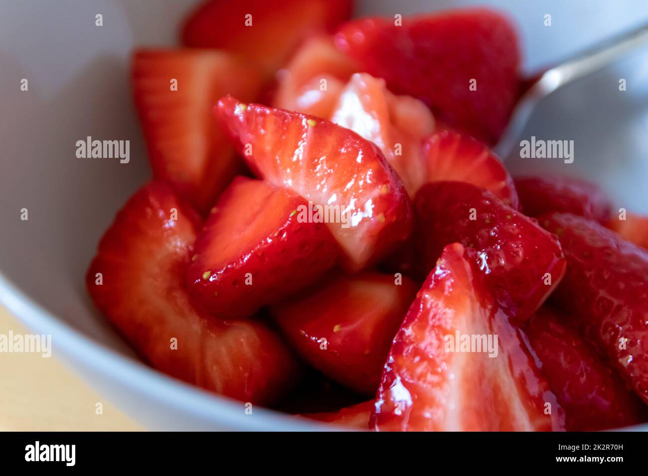 Molte fragole tagliate in ciotola sono pronte a mangiare con cucchiaio d'argento o come delizioso cibo per le dita e uno spuntino sano con frutta rossa e vitamine sul tavolo da cucina in legno per un'alimentazione e una salute sostenibili Foto Stock