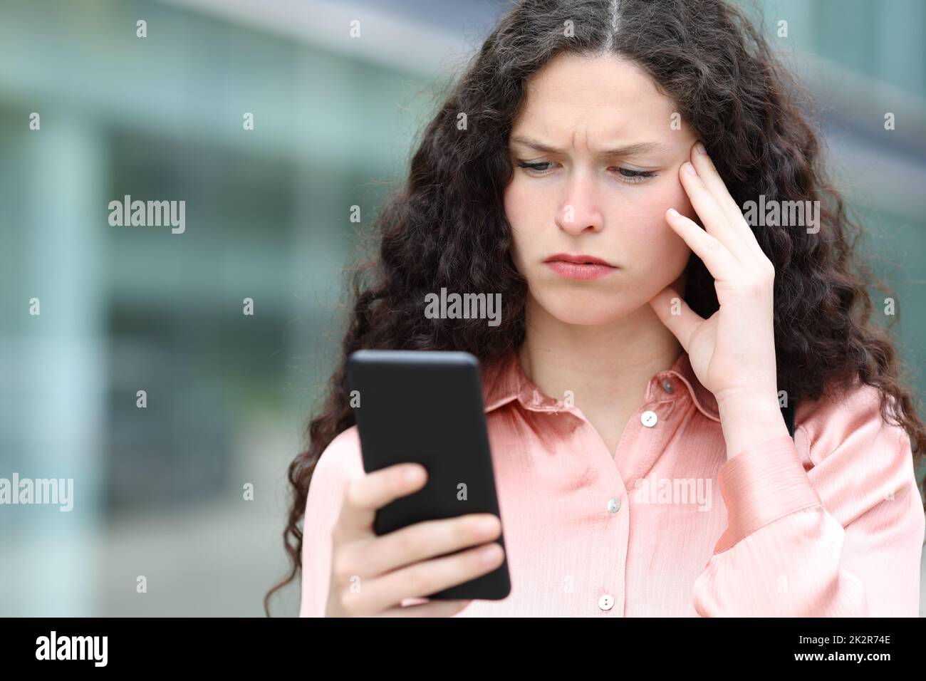 Donna preoccupata che legge il messaggio sul telefono per strada Foto Stock