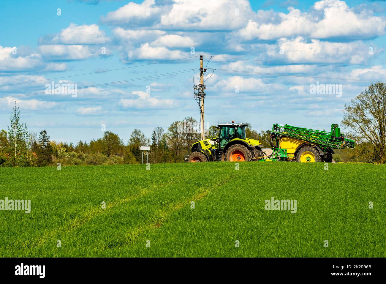 Trattore con irroratrice che passa su campo verde Foto Stock