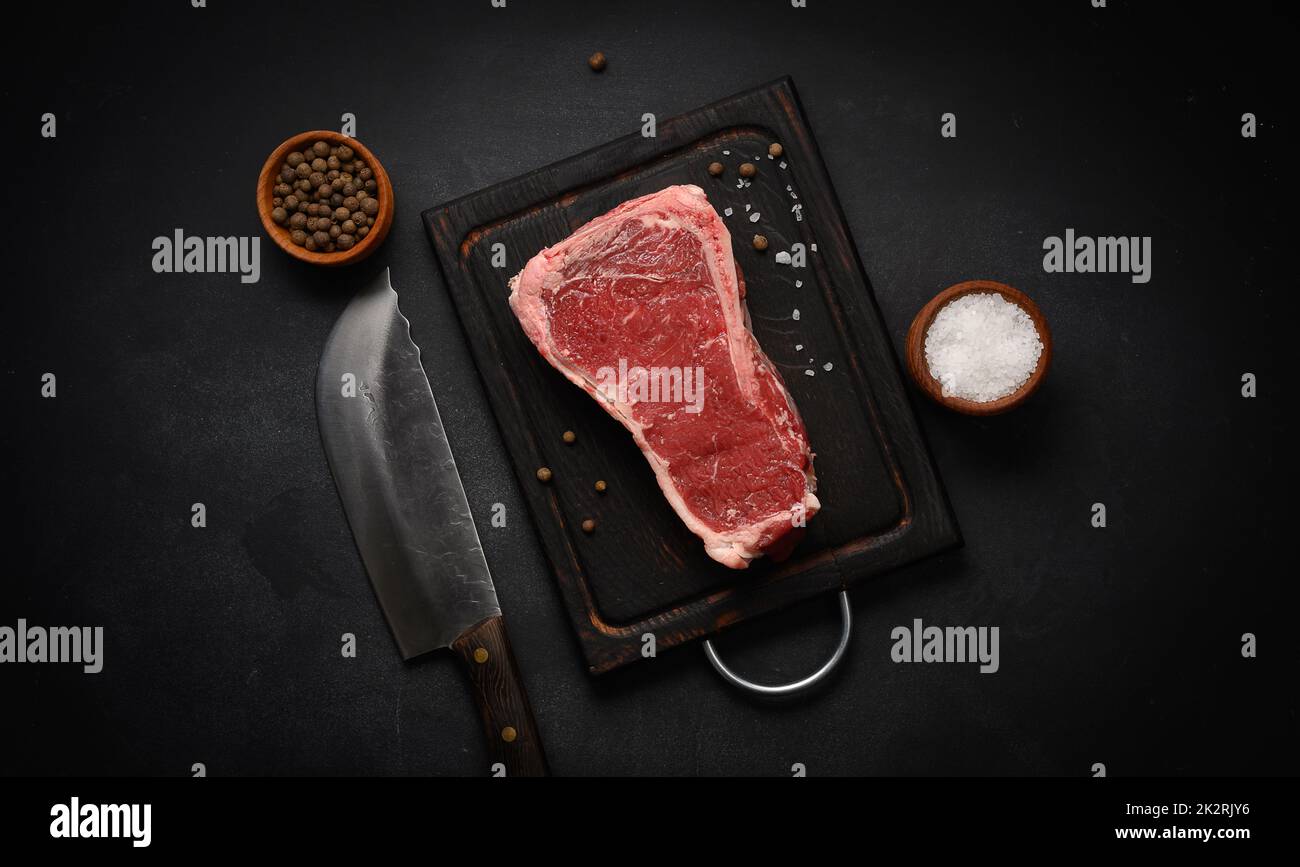 Pezzo fresco di carne di manzo crudo, bistecca striploin su sfondo nero, vista dall'alto. Pezzo marmorizzato di carne New York Foto Stock