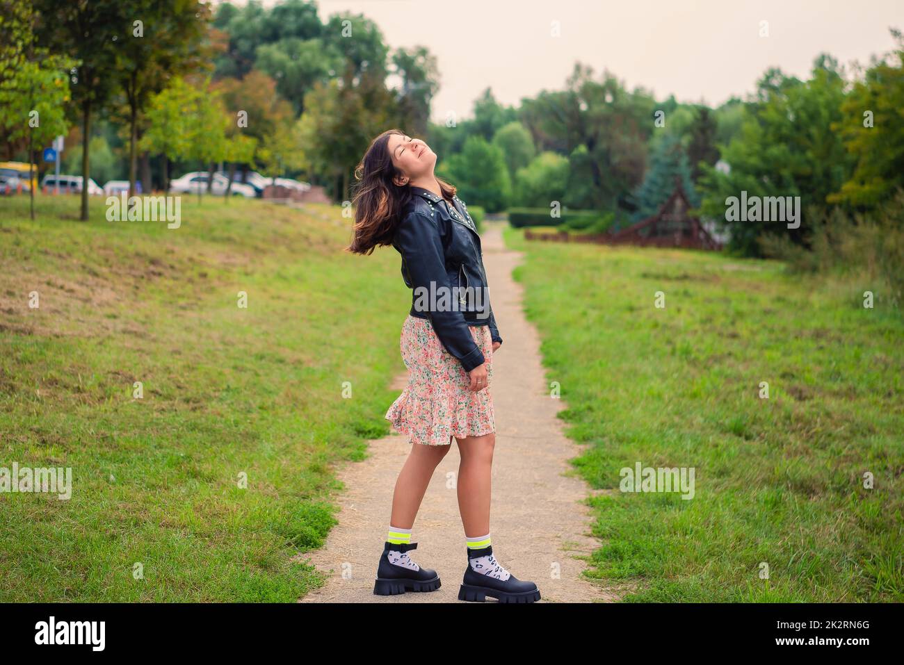 bellissima ragazza sorridendo, chiudendo gli occhi e sollevando la testa in un parco verde Foto Stock